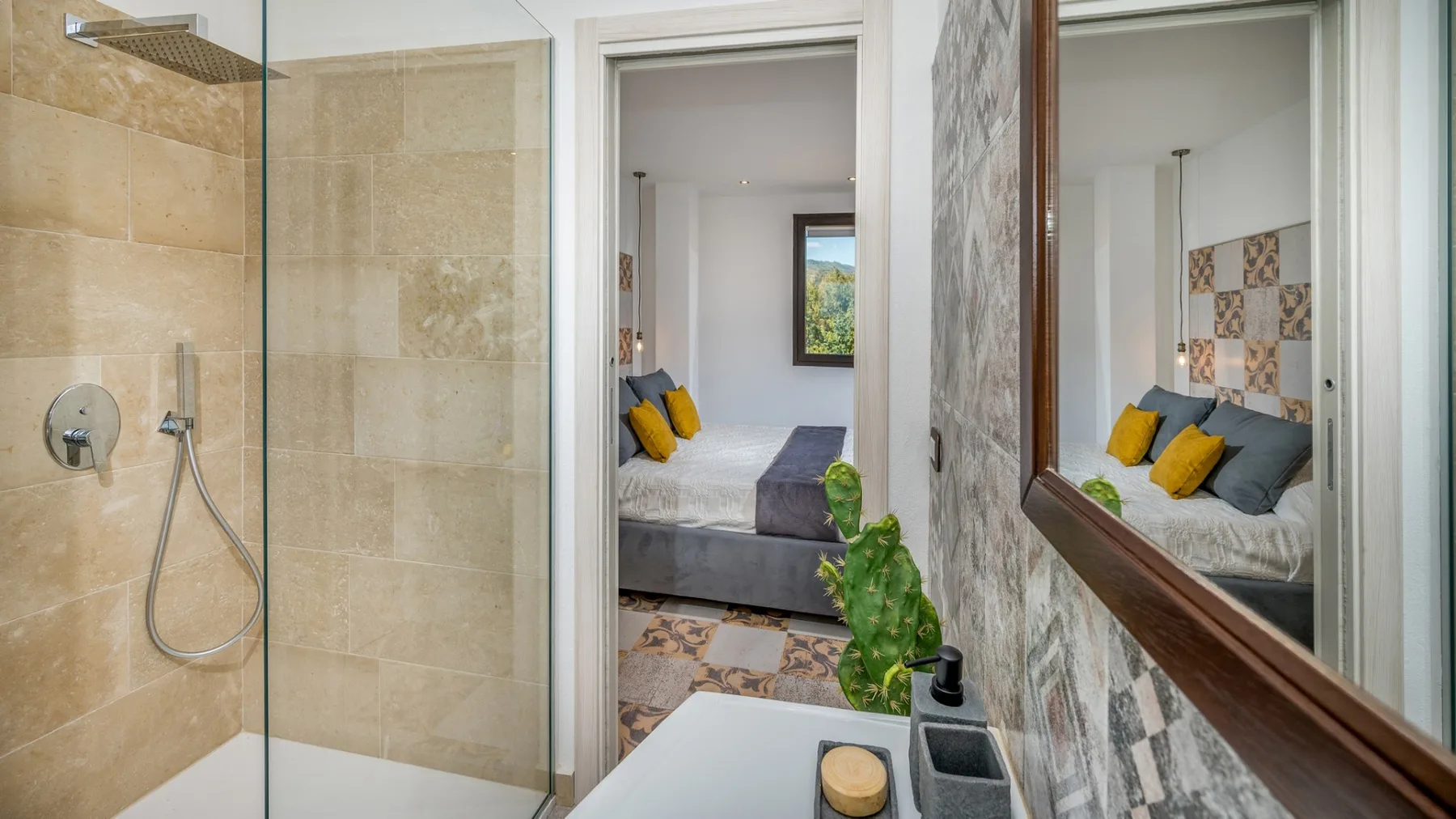 Un baño con ducha de vidrio y un espejo que refleja un dormitorio.