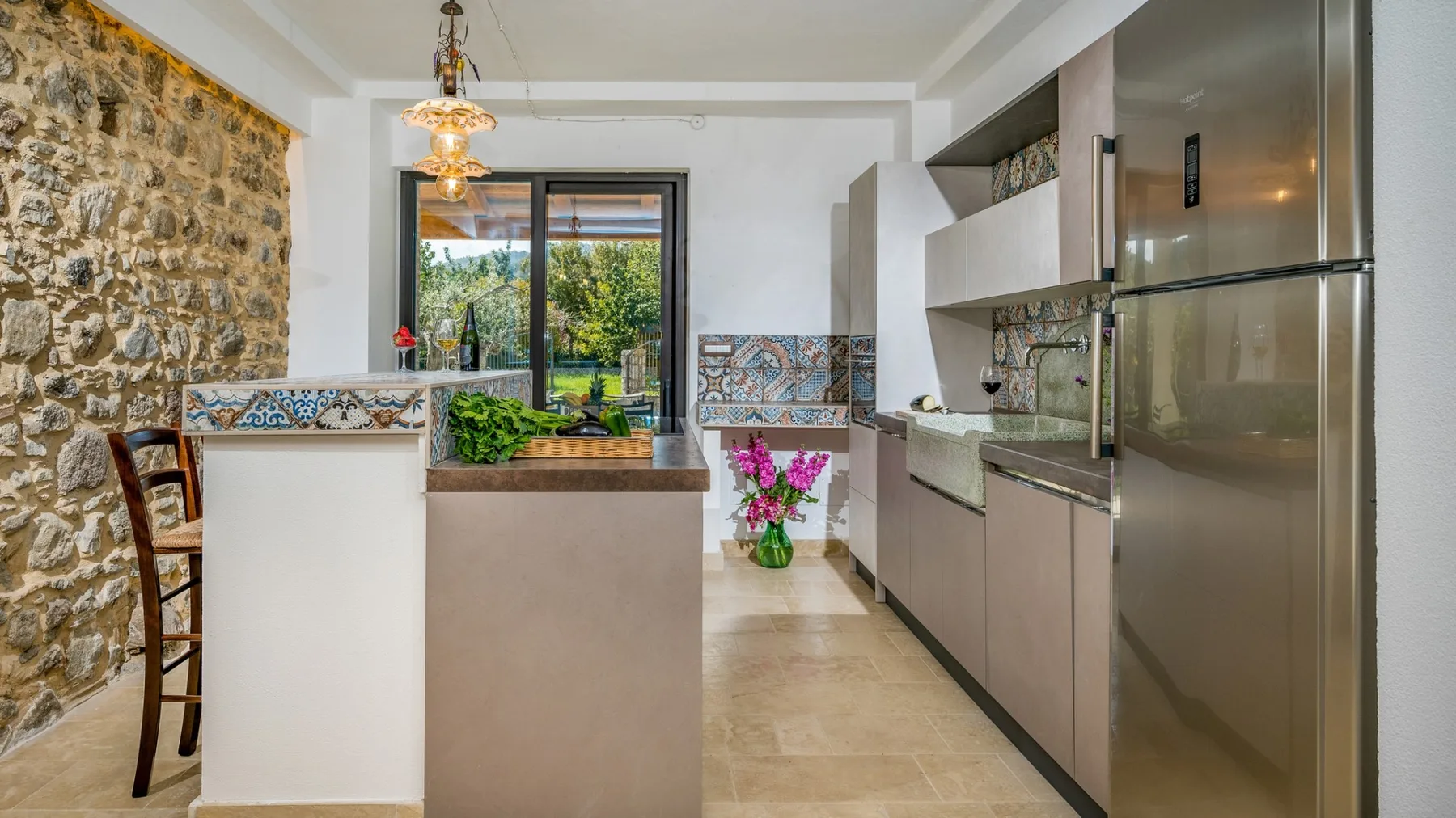 Una cocina moderna con península, pared de piedra y puertas de vidrio con vista a la vegetación.