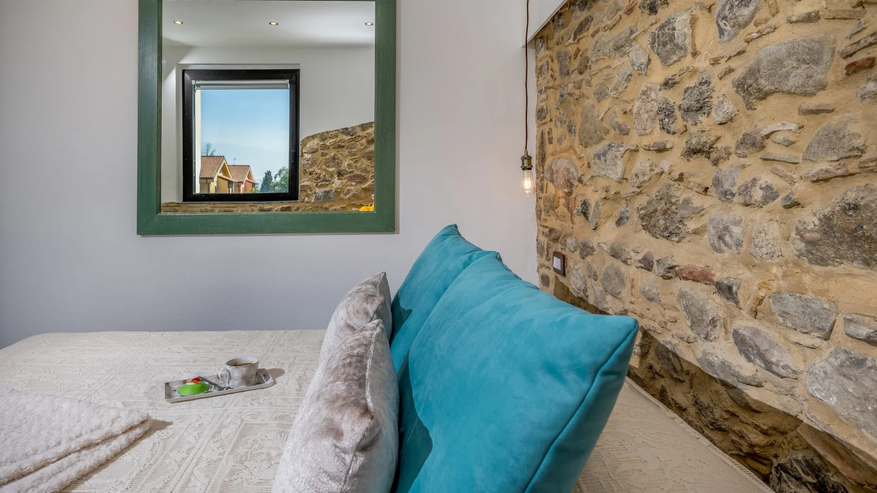 Un dormitorio con una cama, almohadas turquesas y una pared de piedra vista.