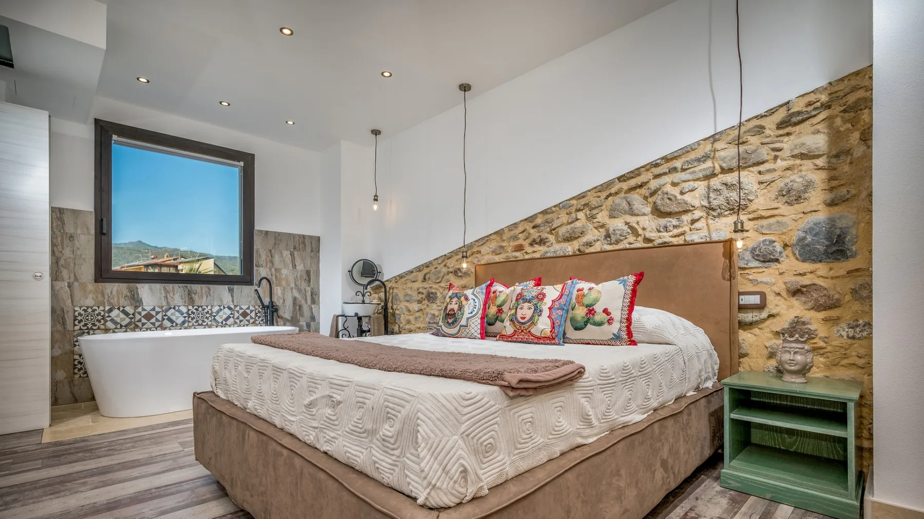 Un dormitorio con una cama grande, cojines coloridos y una ventana con vistas al paisaje.
