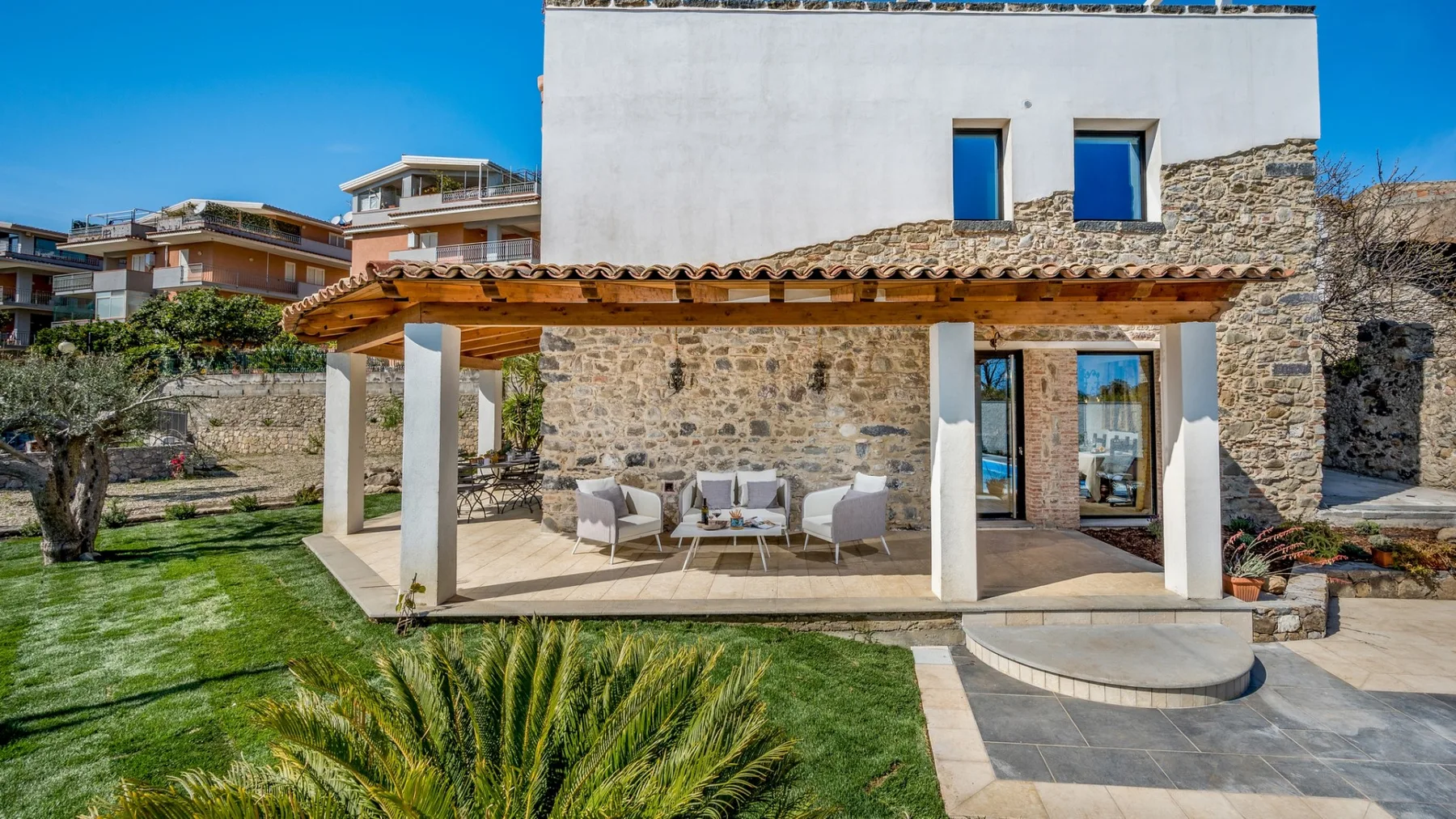 Una casa de piedra con patio cubierto, asientos al aire libre y césped.