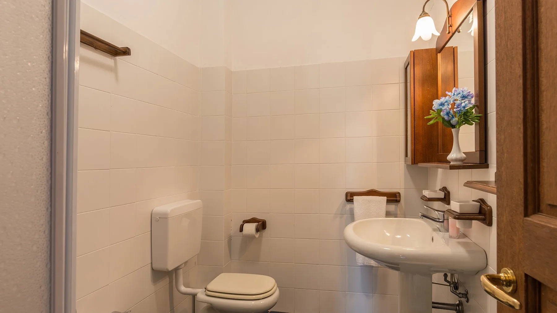 Un baño con azulejos, un inodoro y un lavabo bajo un espejo.