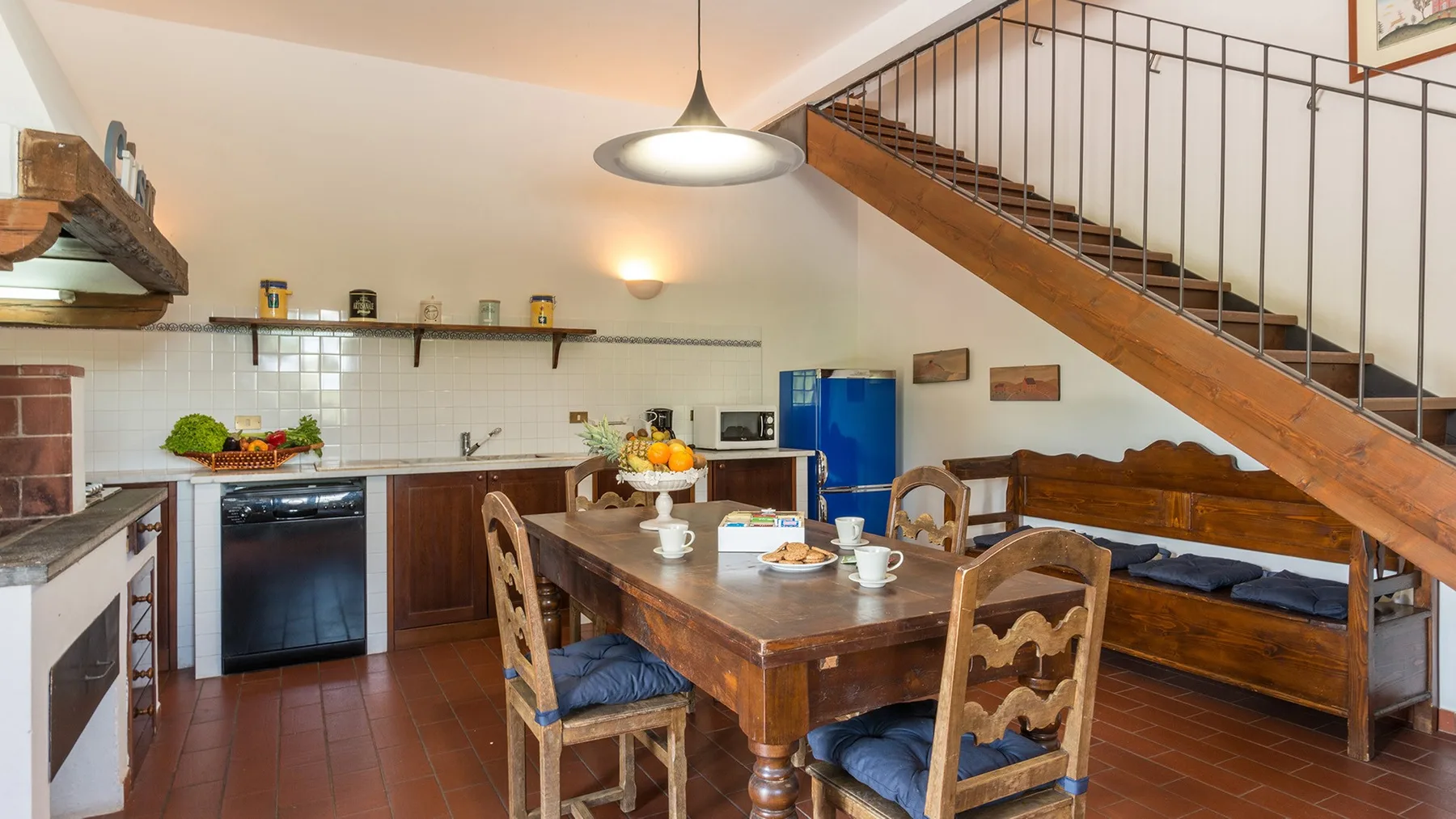 Una cocina y comedor con una mesa de madera bajo una escalera.