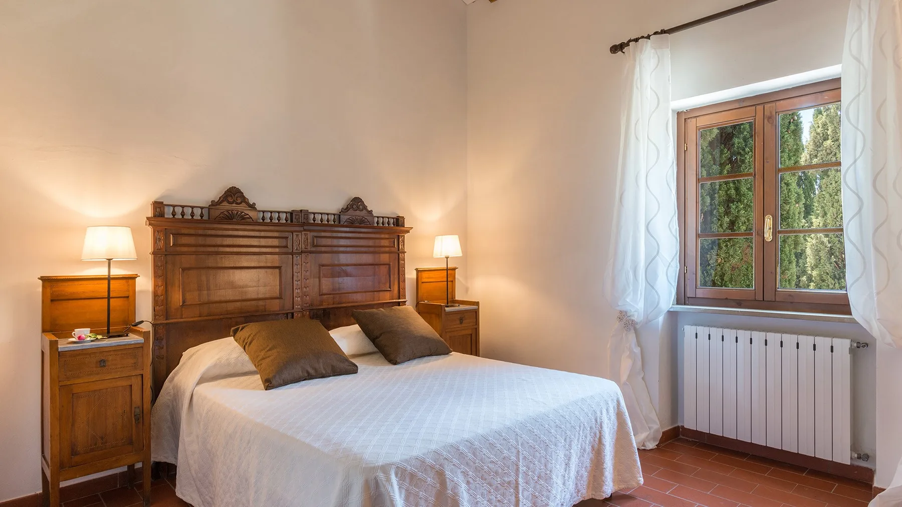 Un dormitorio con una cama bien tendida y una ventana con cortinas blancas.