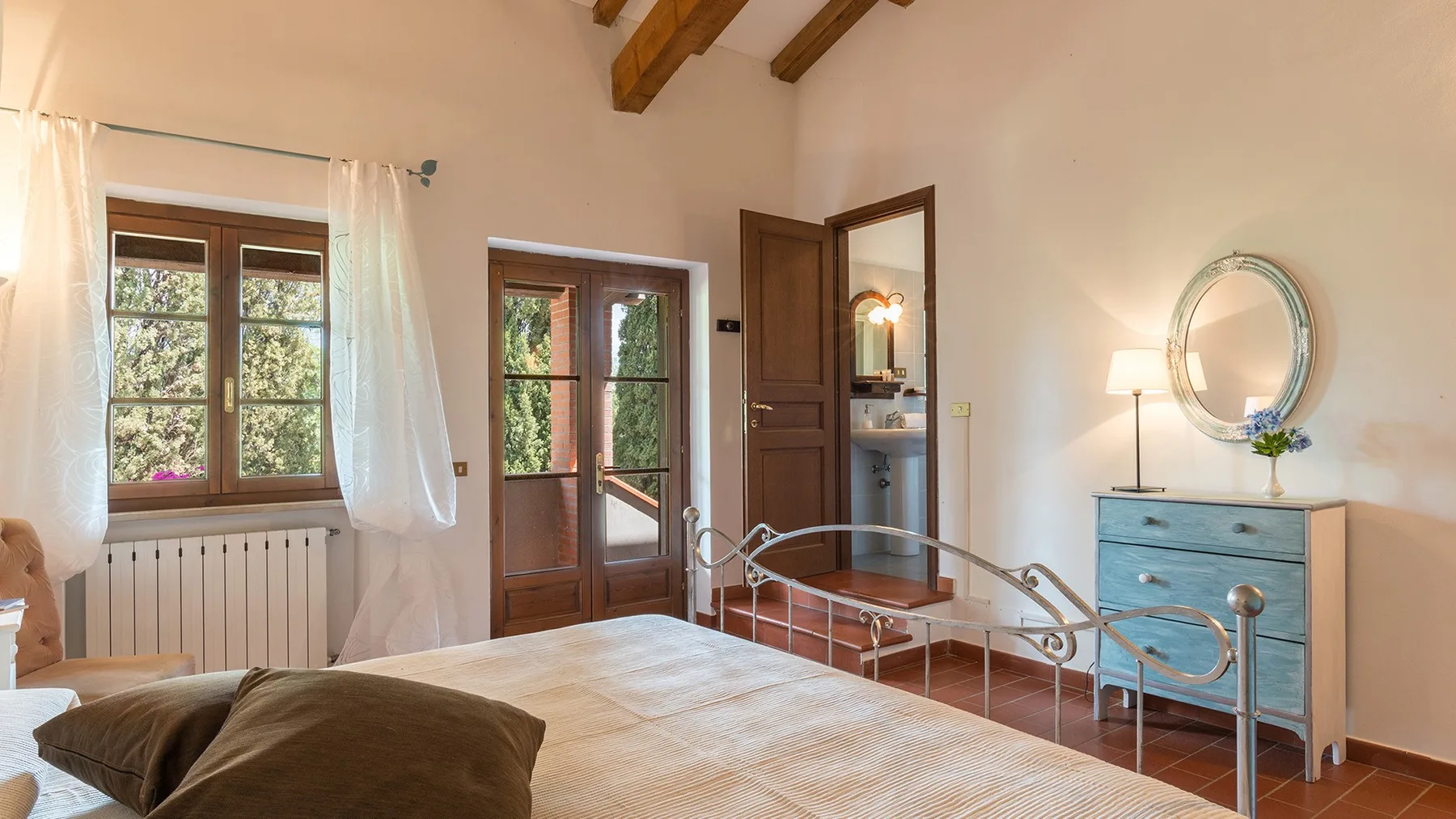 Un dormitorio con una cama, ventanas con marcos de madera y una cómoda azul.