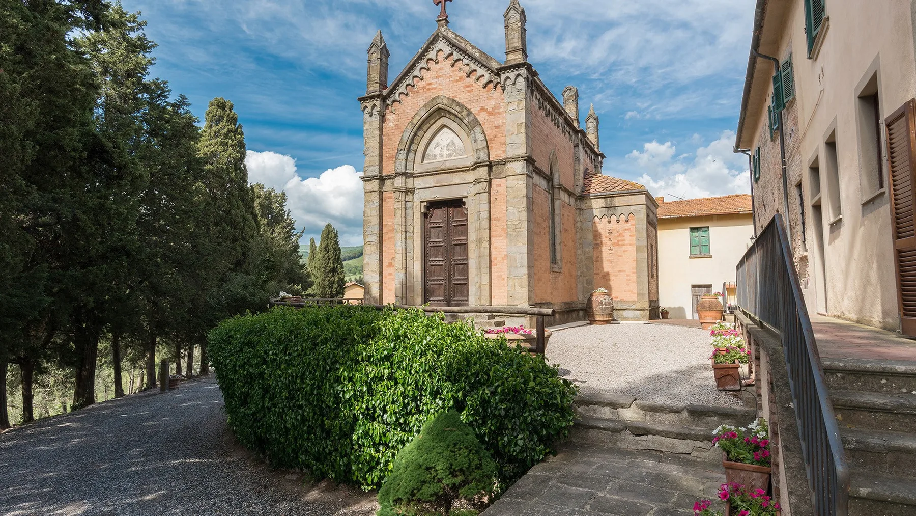 Una pequeña iglesia de piedra se alza junto a un patio de grava con setos verdes.