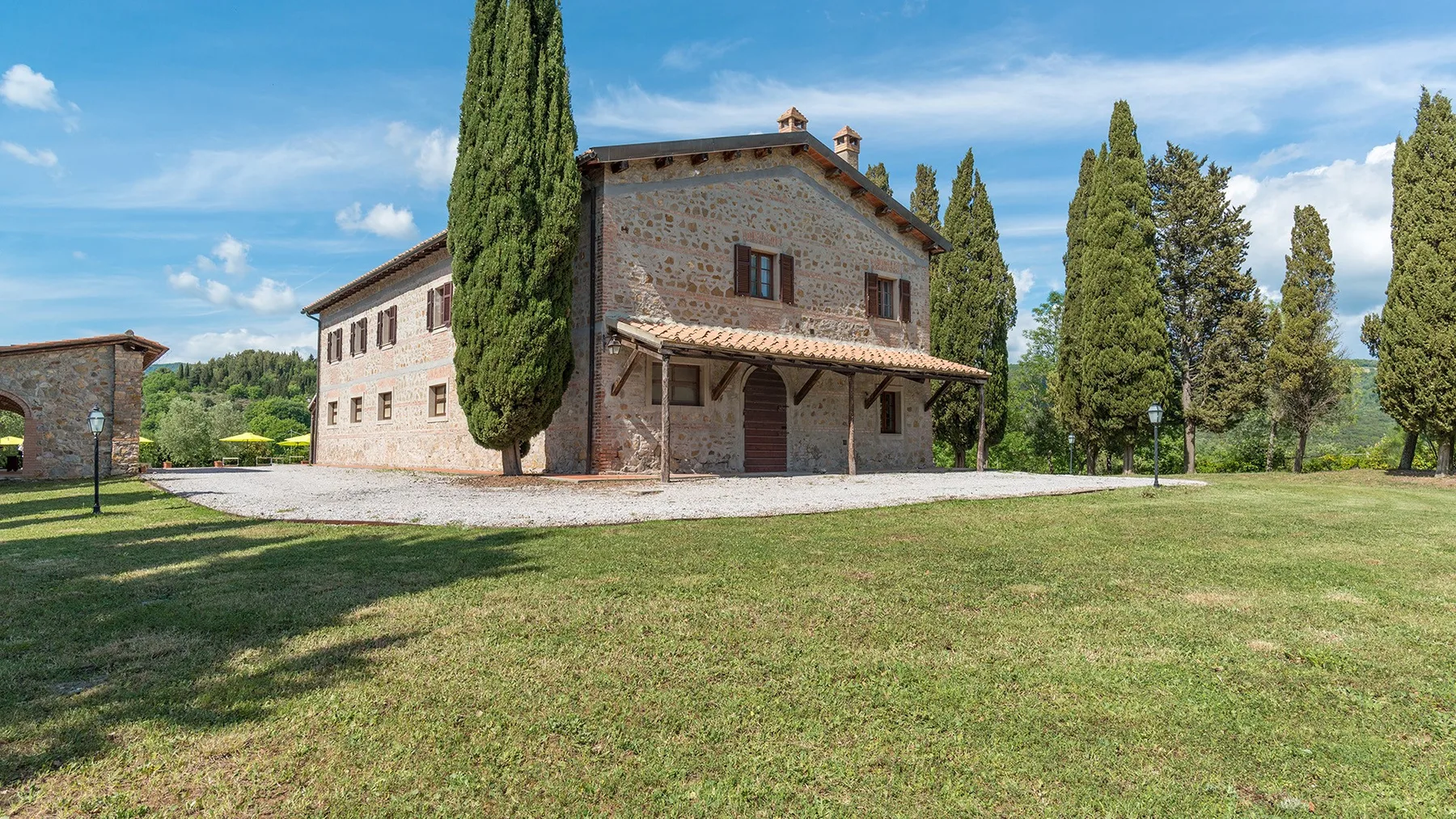 Una casa de piedra se alza junto a un amplio césped y árboles altos.