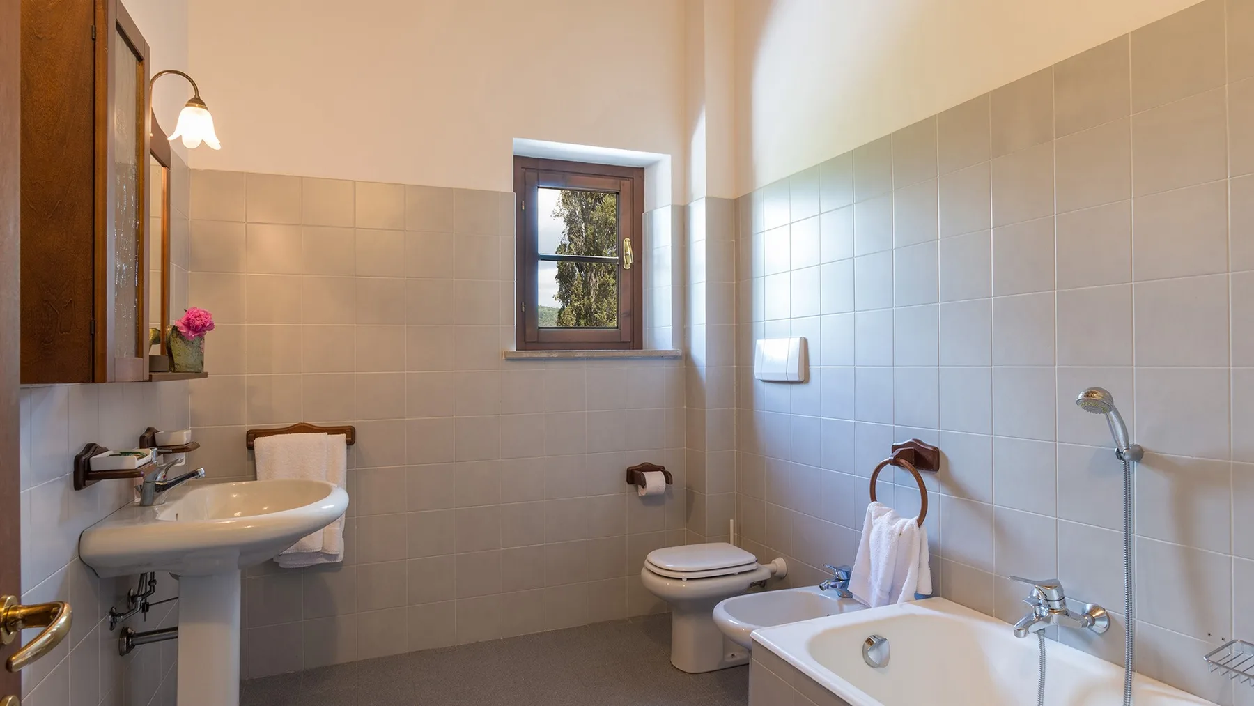Un baño alicatado con bañera, lavabo y una ventana pequeña.