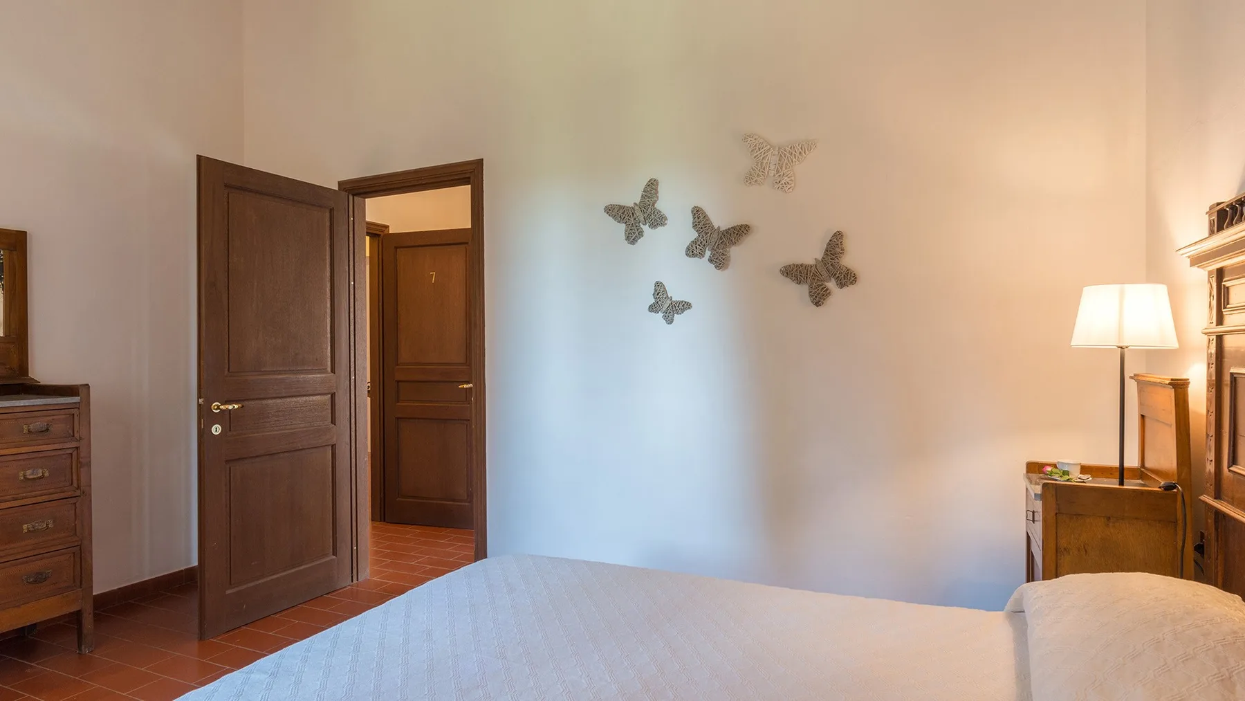 Un dormitorio con una cama, una puerta de madera abierta y adornos de mariposas en la pared.