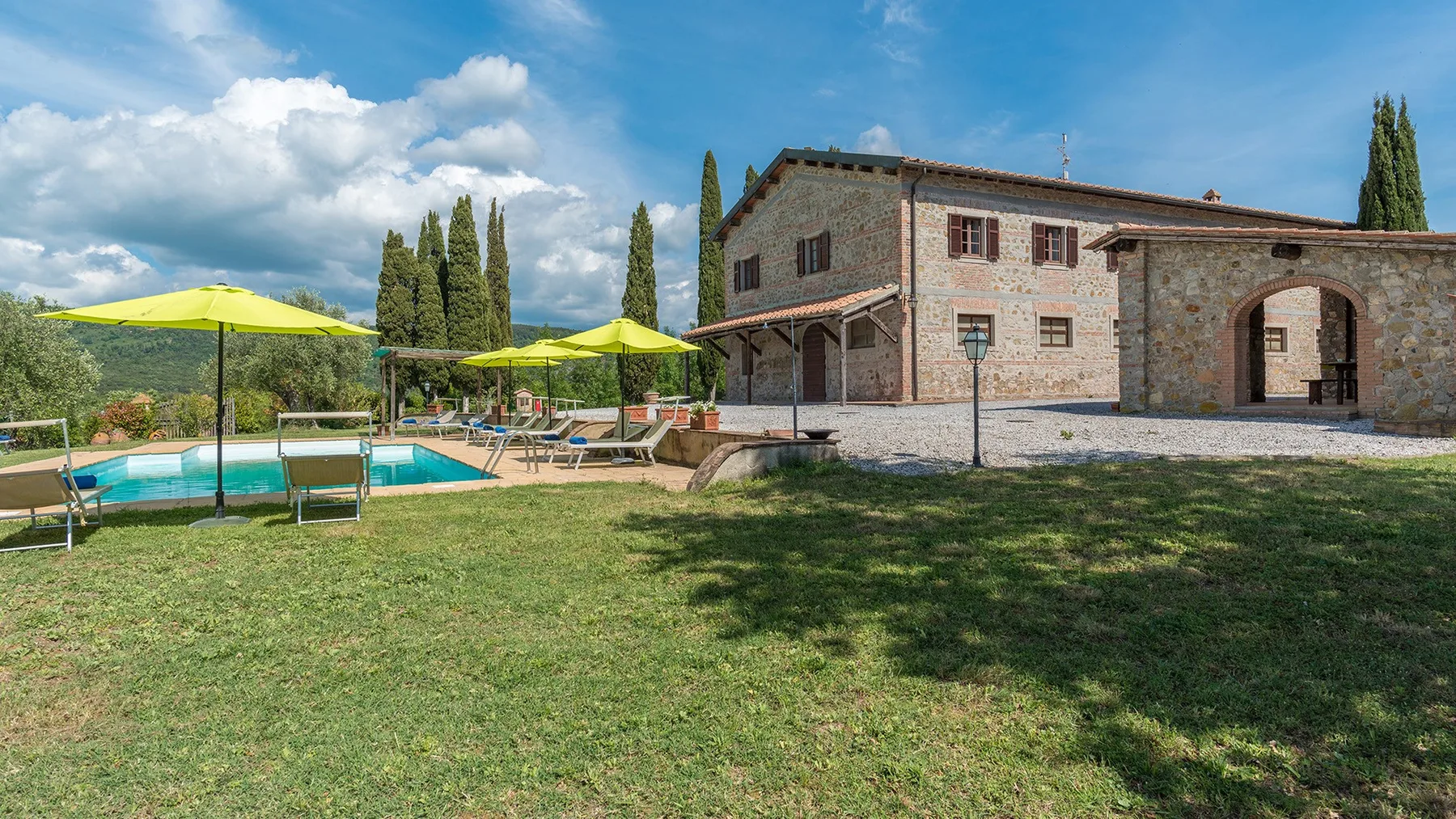 Una casa de piedra se alza junto a una piscina y un césped.