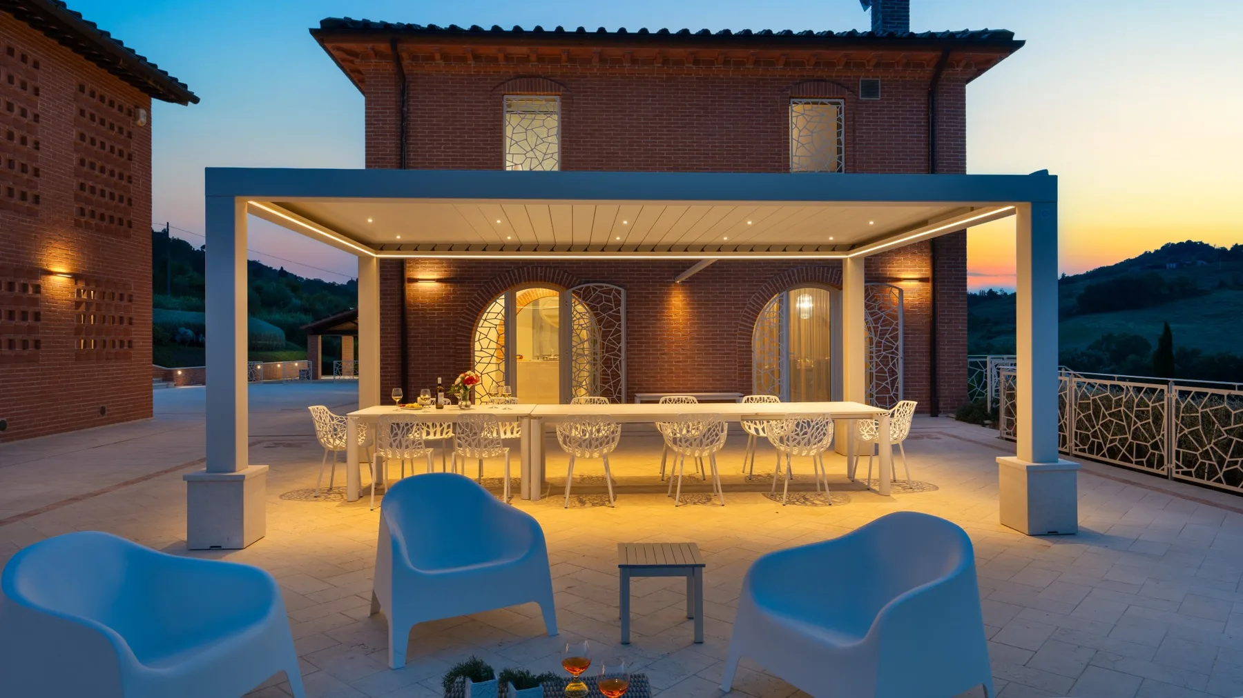 An outdoor dining area under a covered patio, with a long table and blue seating.