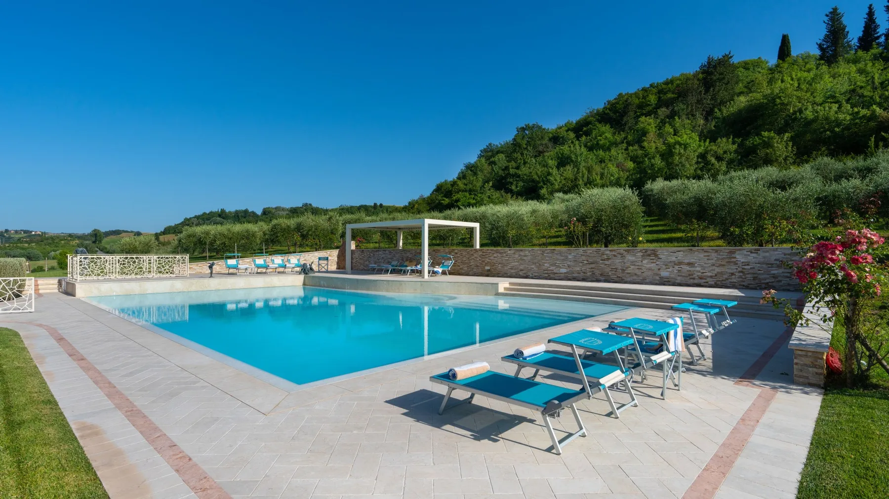 An outdoor swimming pool with lounge seating beside a green hillside.