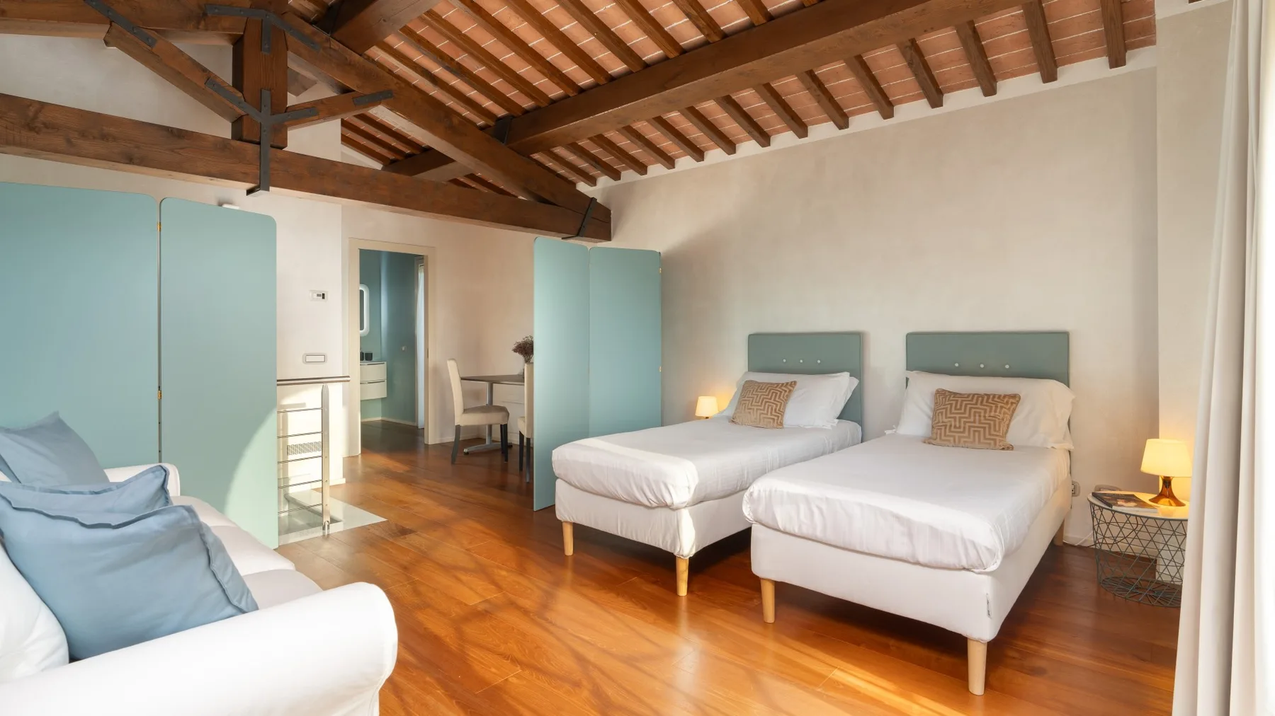 A bedroom with two beds, wooden flooring, and exposed ceiling beams.