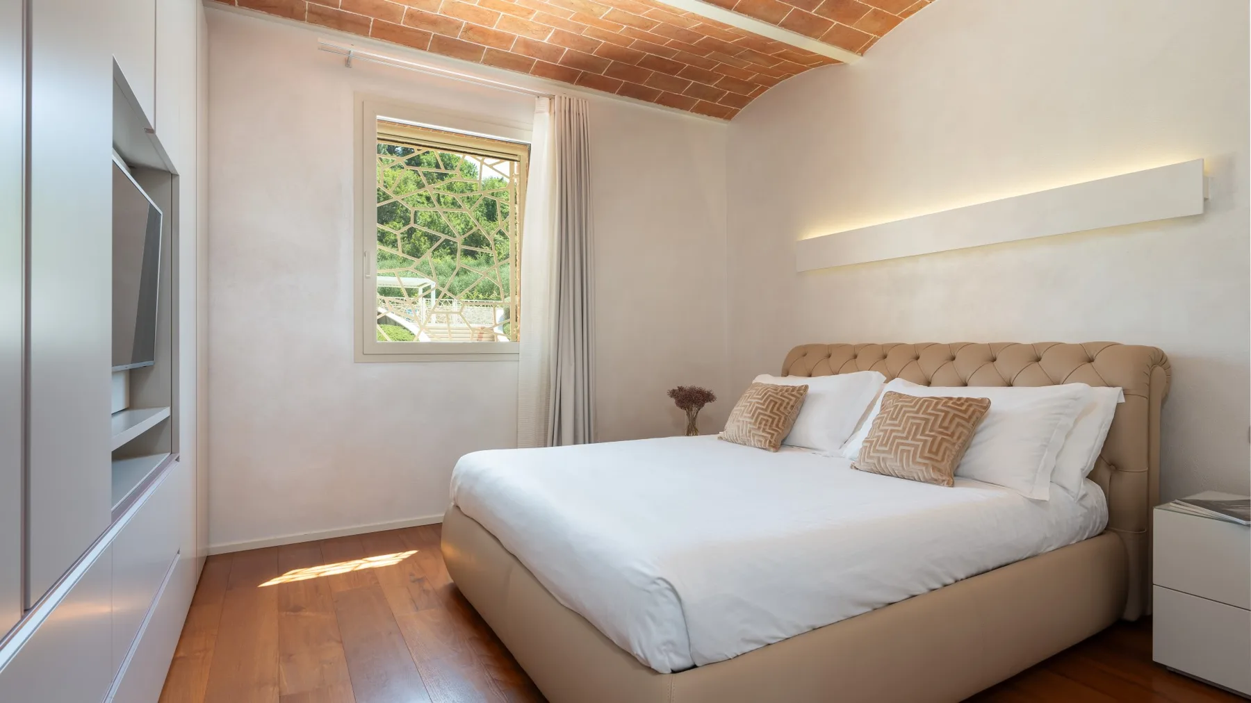 A bedroom with a large bed, a window, and a brick ceiling.