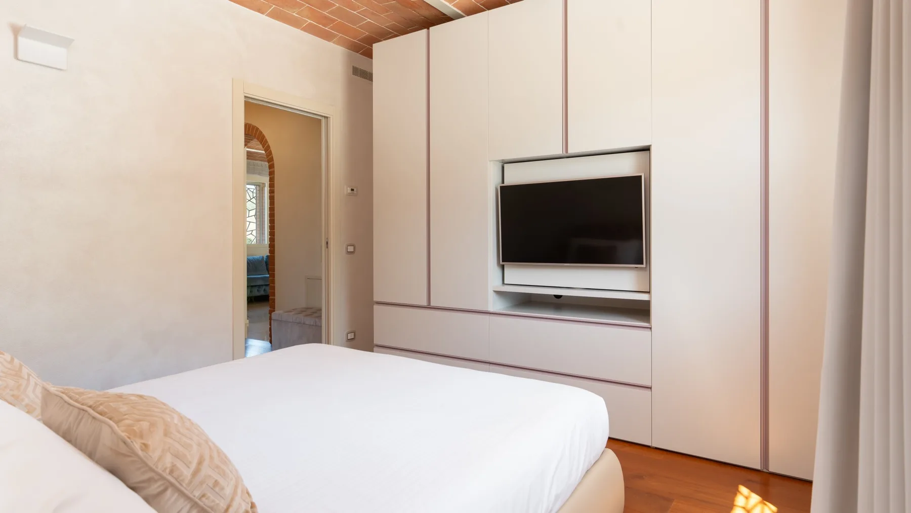 A bedroom with a neatly made bed and a television mounted on built-in cabinetry.