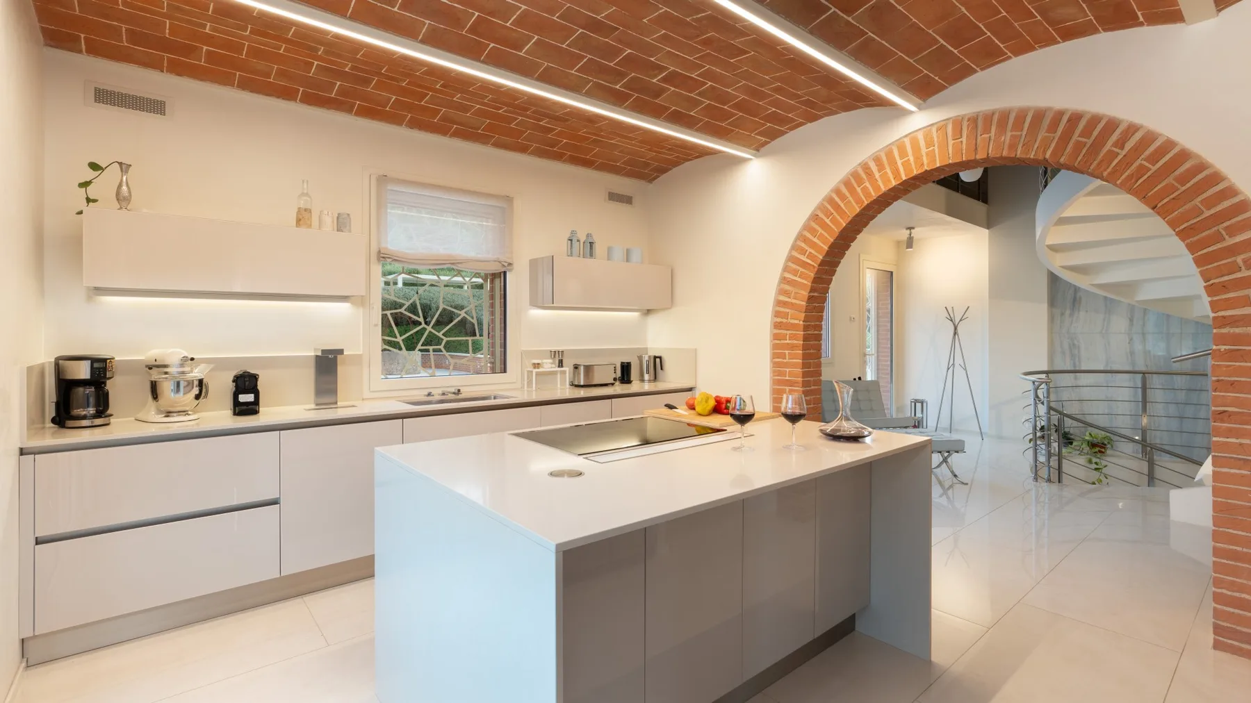 A modern kitchen with a large central island and a brick archway.