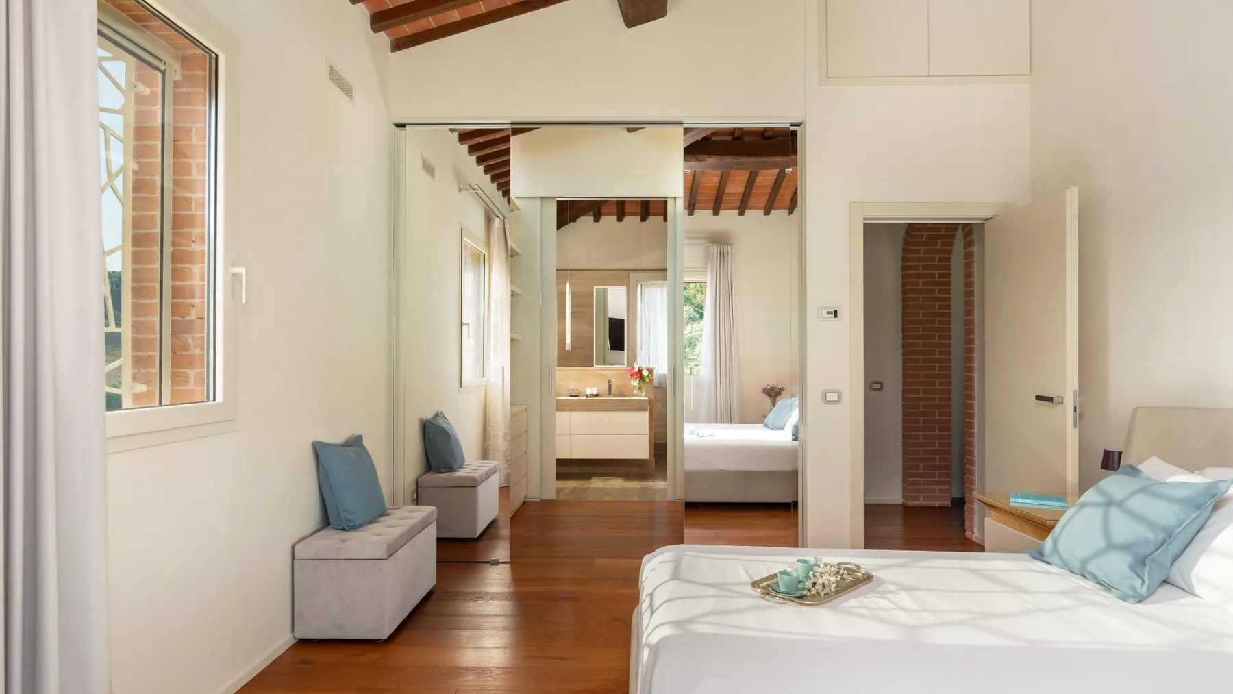 A bright bedroom with a large bed and a mirrored wall.