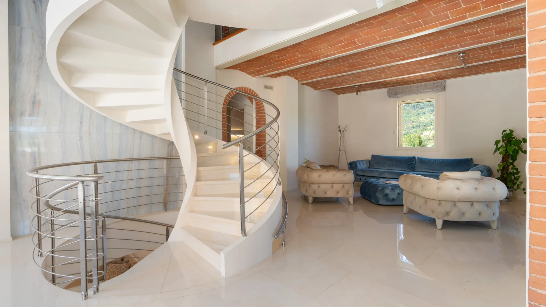 A bright living room with a curved staircase and blue seating.