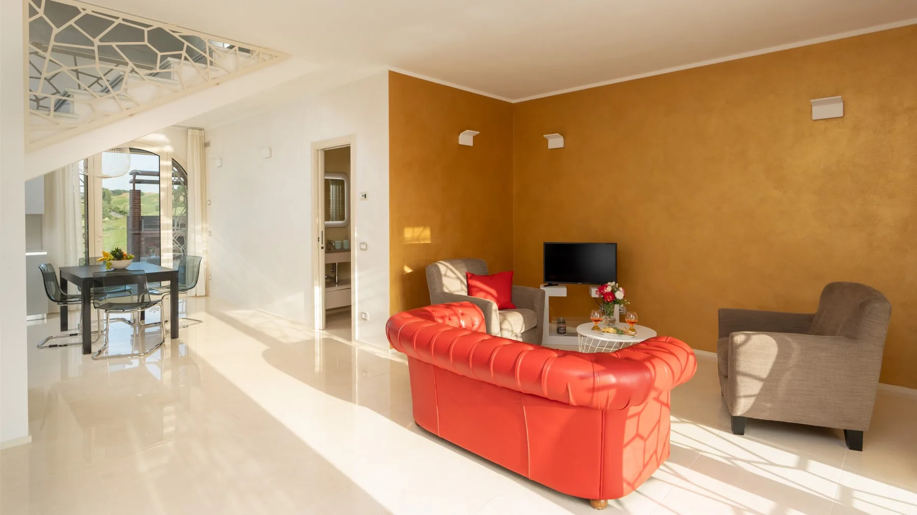A bright living room with red seating, a television, and a dining area beyond.