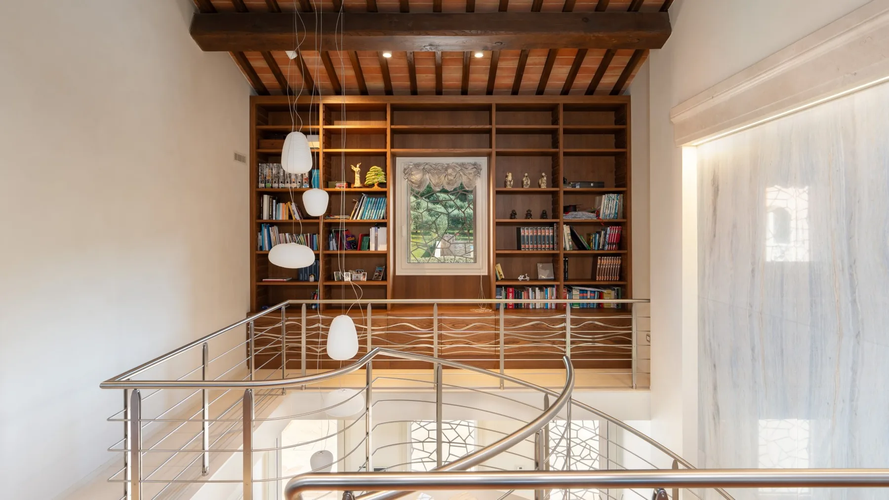 A loft landing overlooks built-in bookshelves beneath exposed wooden ceiling beams.