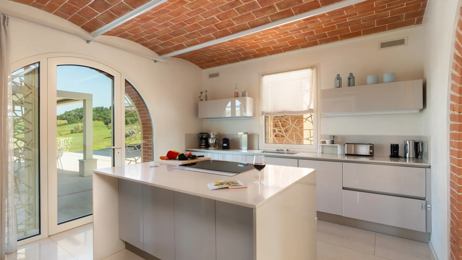 A bright kitchen with a central island, pale cabinets, and a brick ceiling.