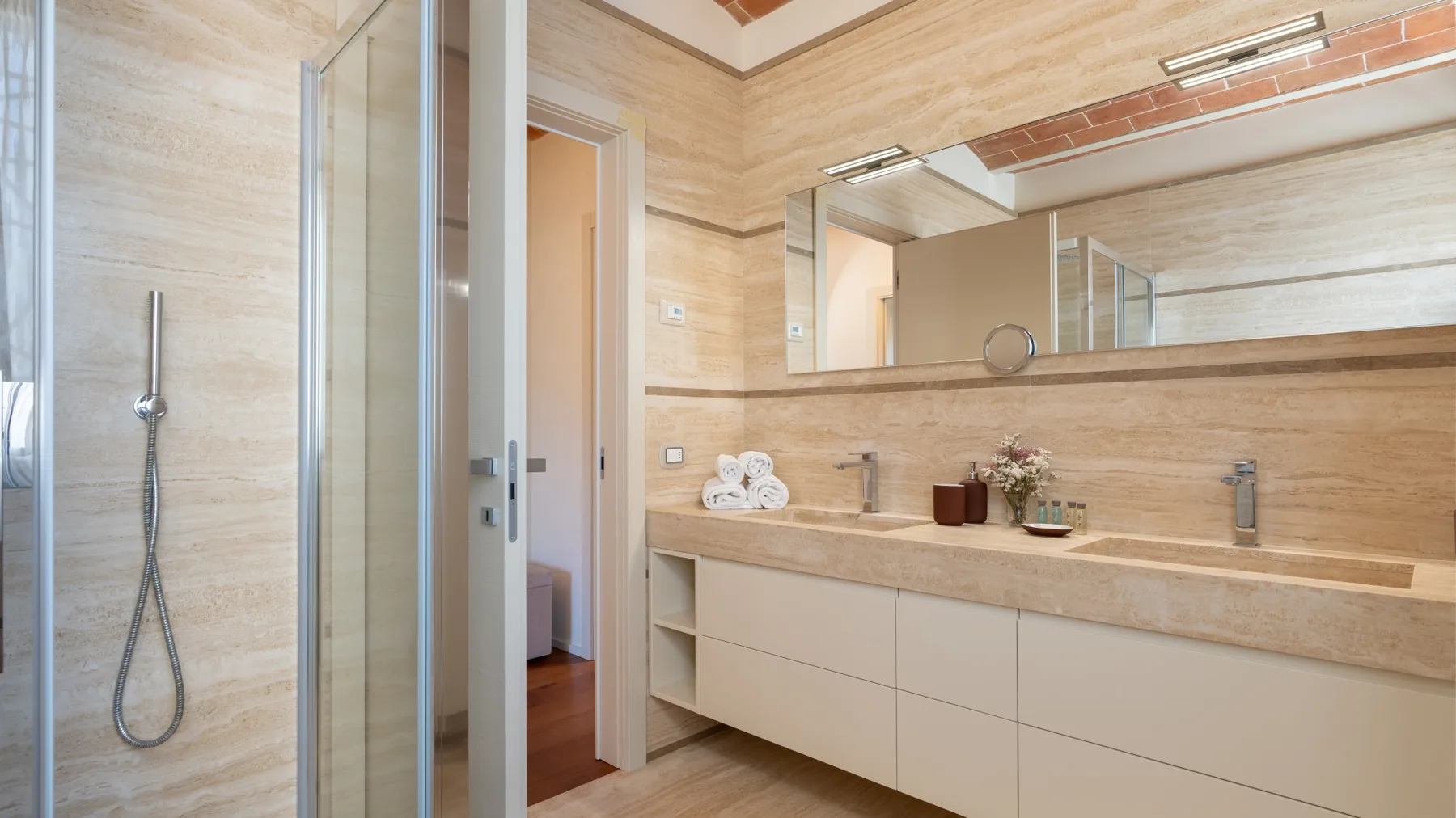 A bright bathroom with a glass shower, long vanity, and wide wall mirror.