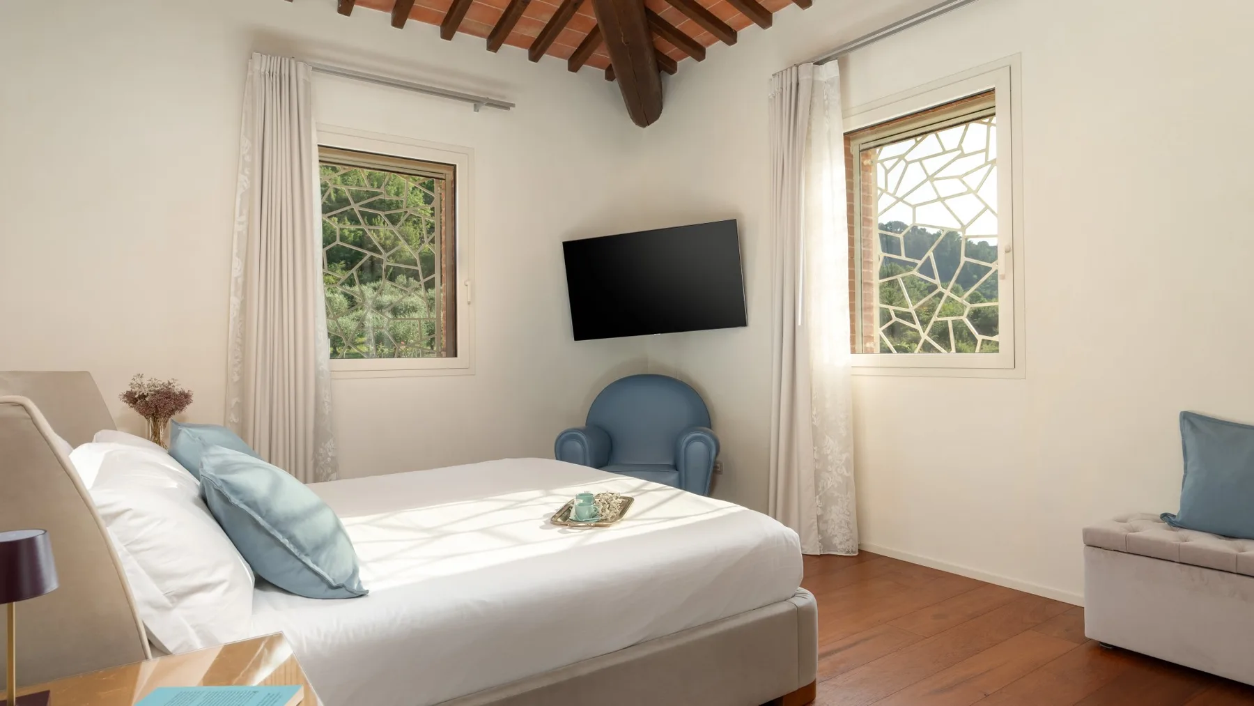 A bedroom with a bed, a blue armchair, and a wall-mounted television.