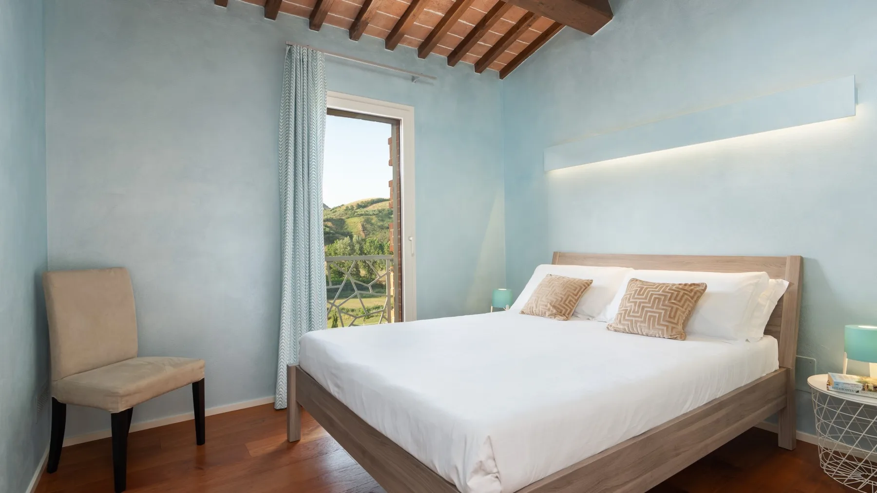A bedroom with a large bed, a chair, and a window overlooking greenery.