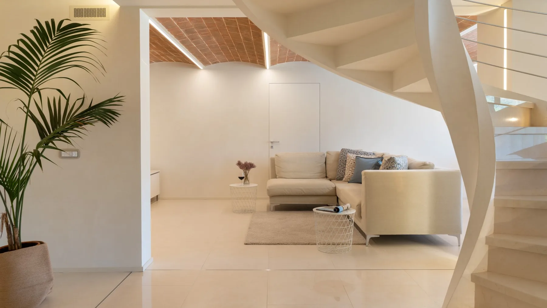 A bright living room with seating beneath a staircase and a potted plant.