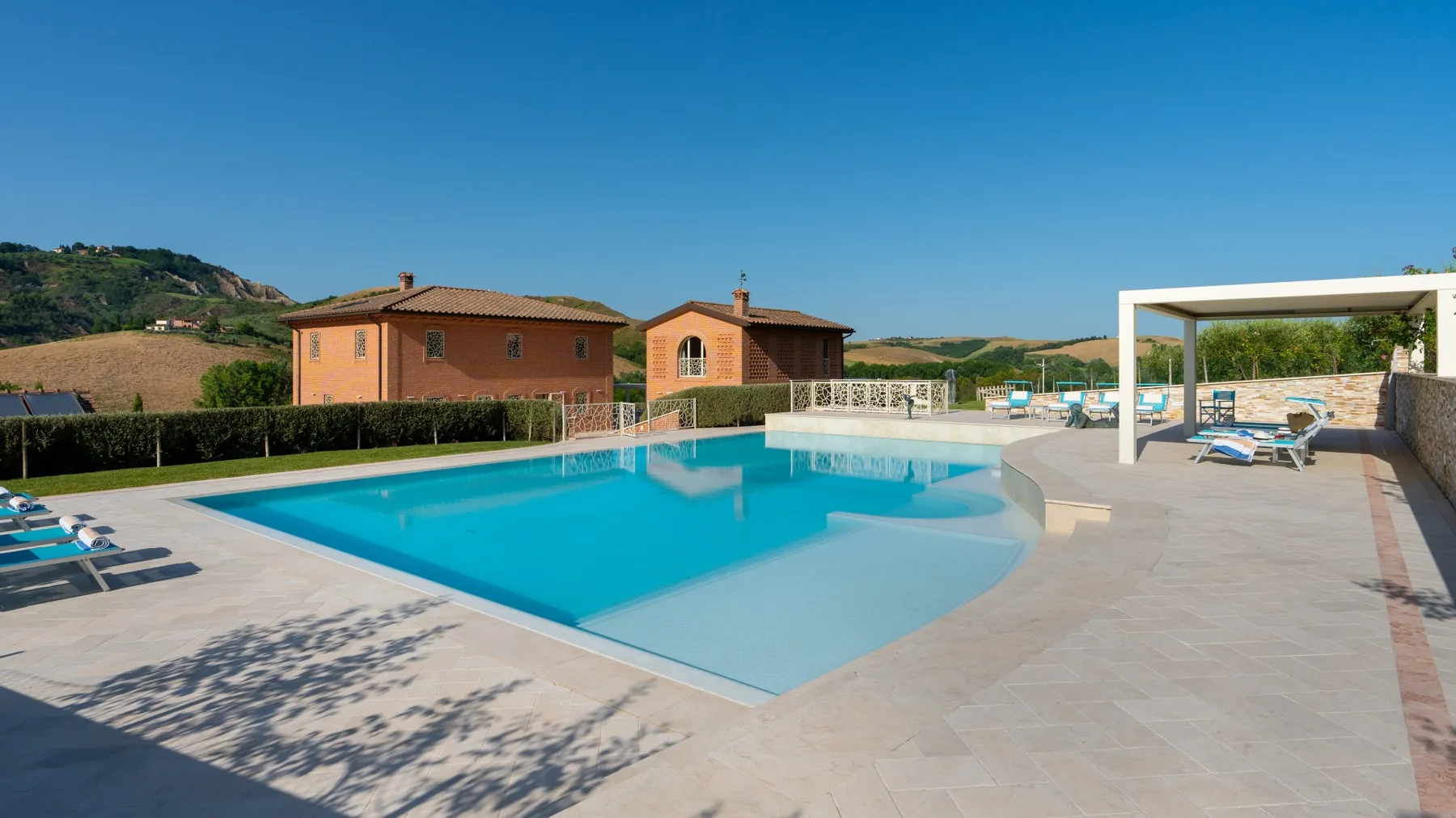 A swimming pool and tiled deck sit beside a shaded seating area.