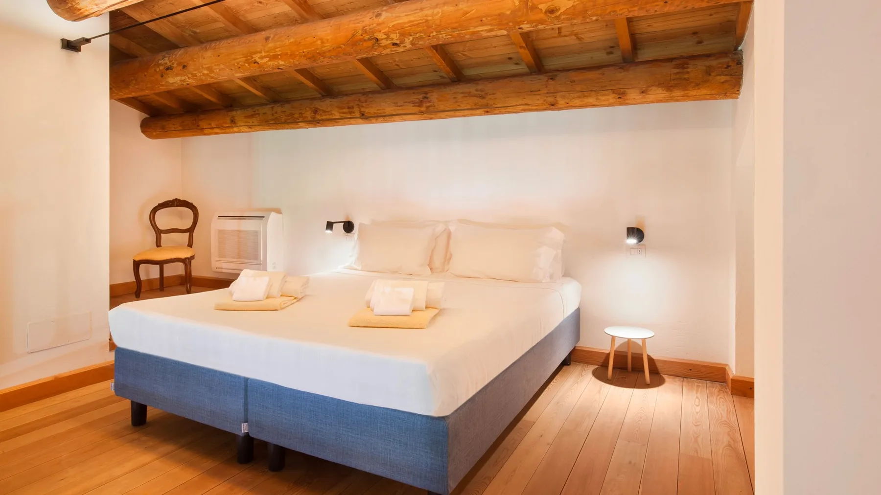 A bedroom with a large bed beneath exposed wooden ceiling beams.