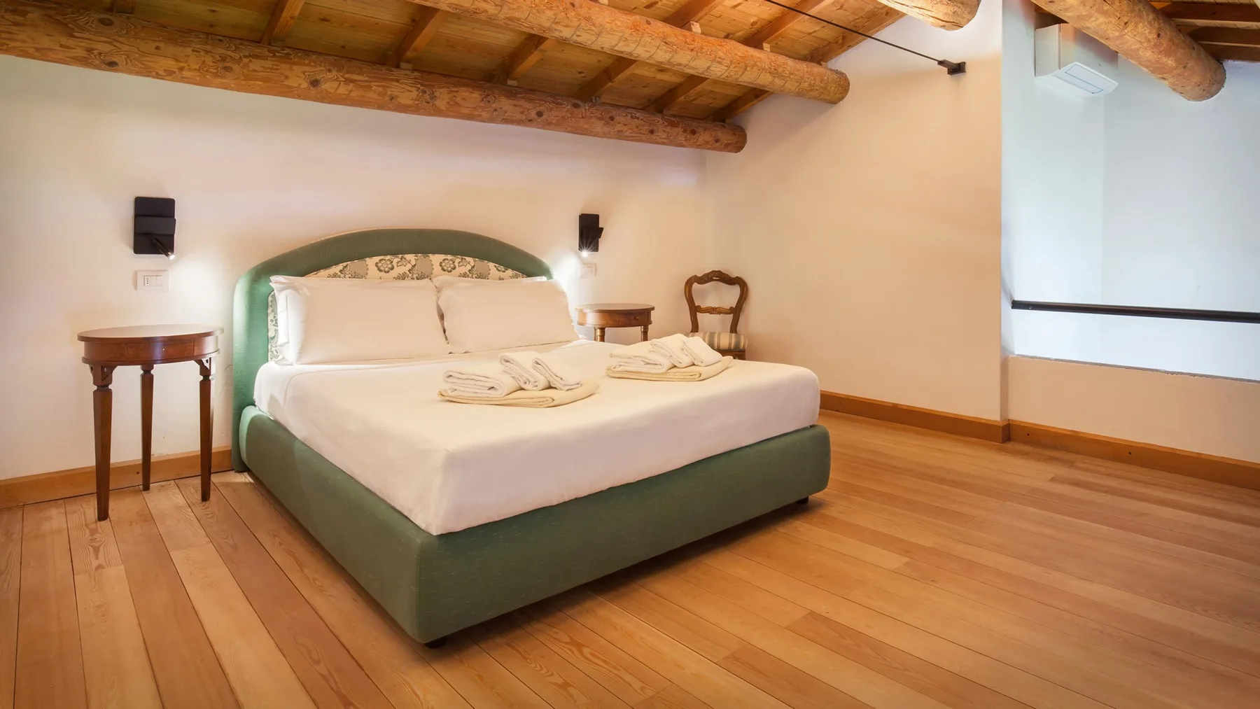 A bedroom with a green bed, white linens, and exposed wooden ceiling beams.