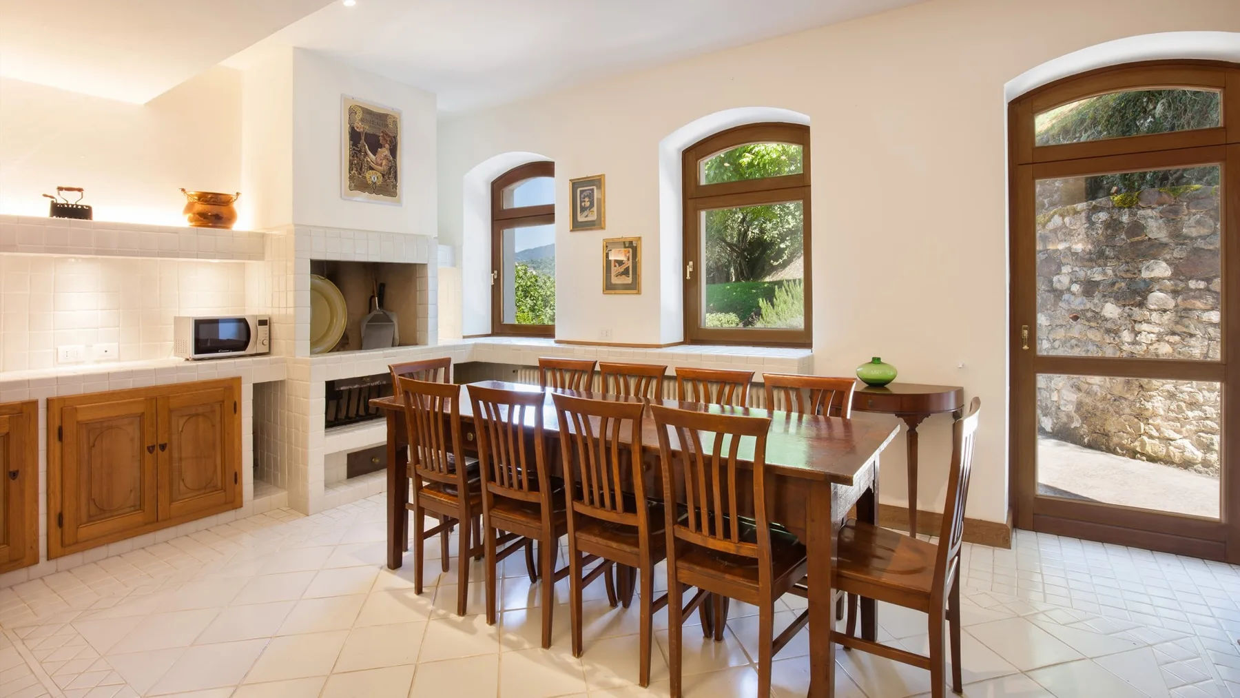 A bright dining room with a long wooden table beside a tiled kitchen counter.