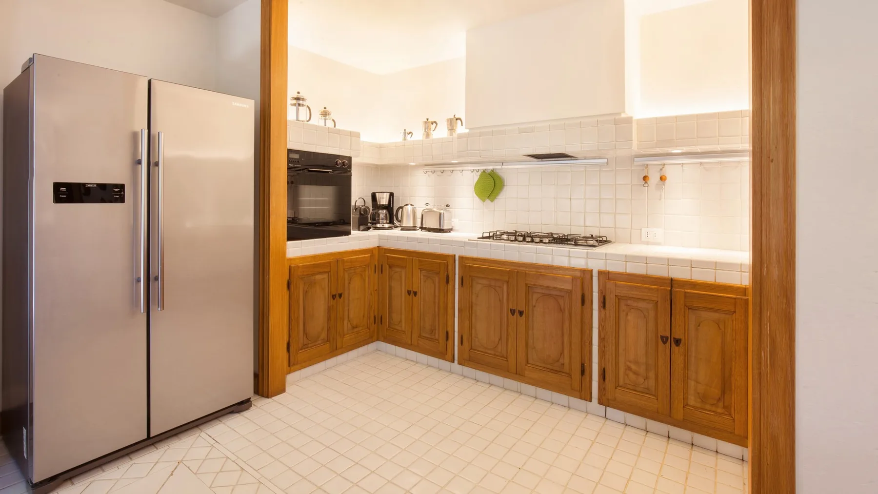 A kitchen with wooden cabinets, a stainless steel refrigerator, and a tiled floor.