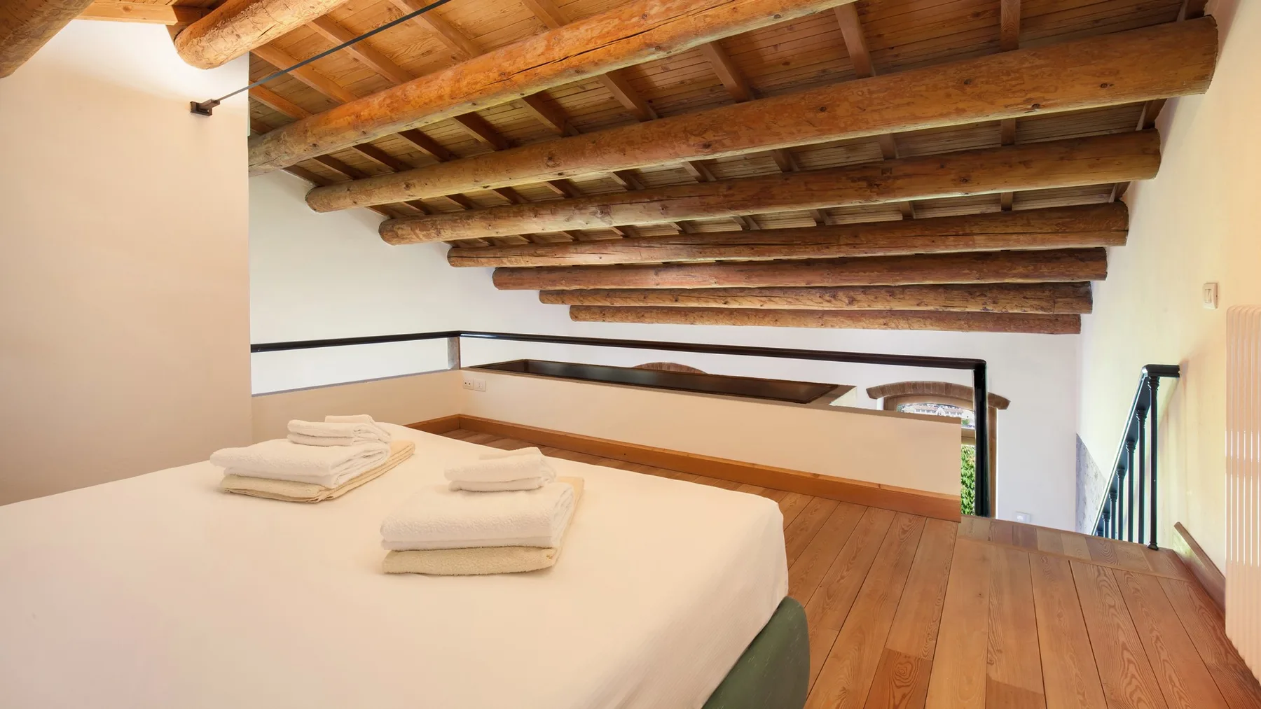 A bedroom with a bed beneath exposed wooden ceiling beams.