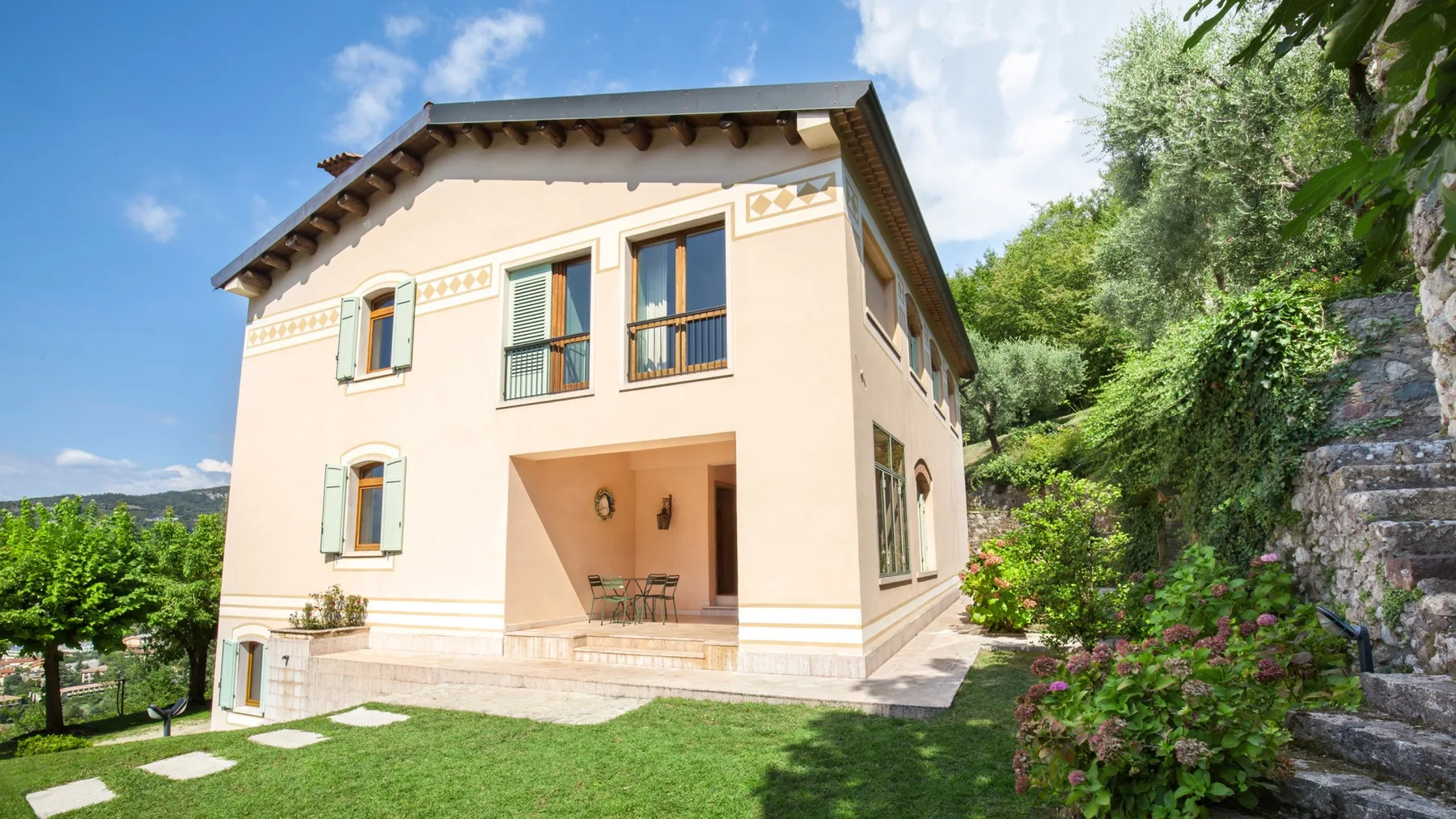 A pale stucco house with a covered patio faces a lawn and garden.