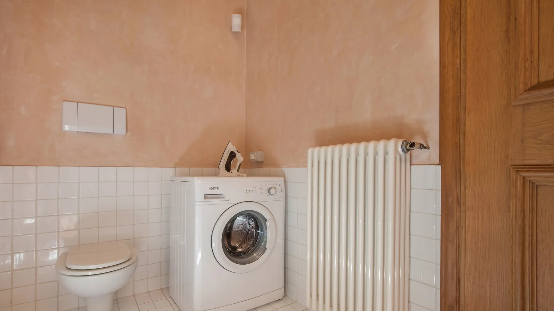 A tiled bathroom with a toilet, washing machine, and radiator.