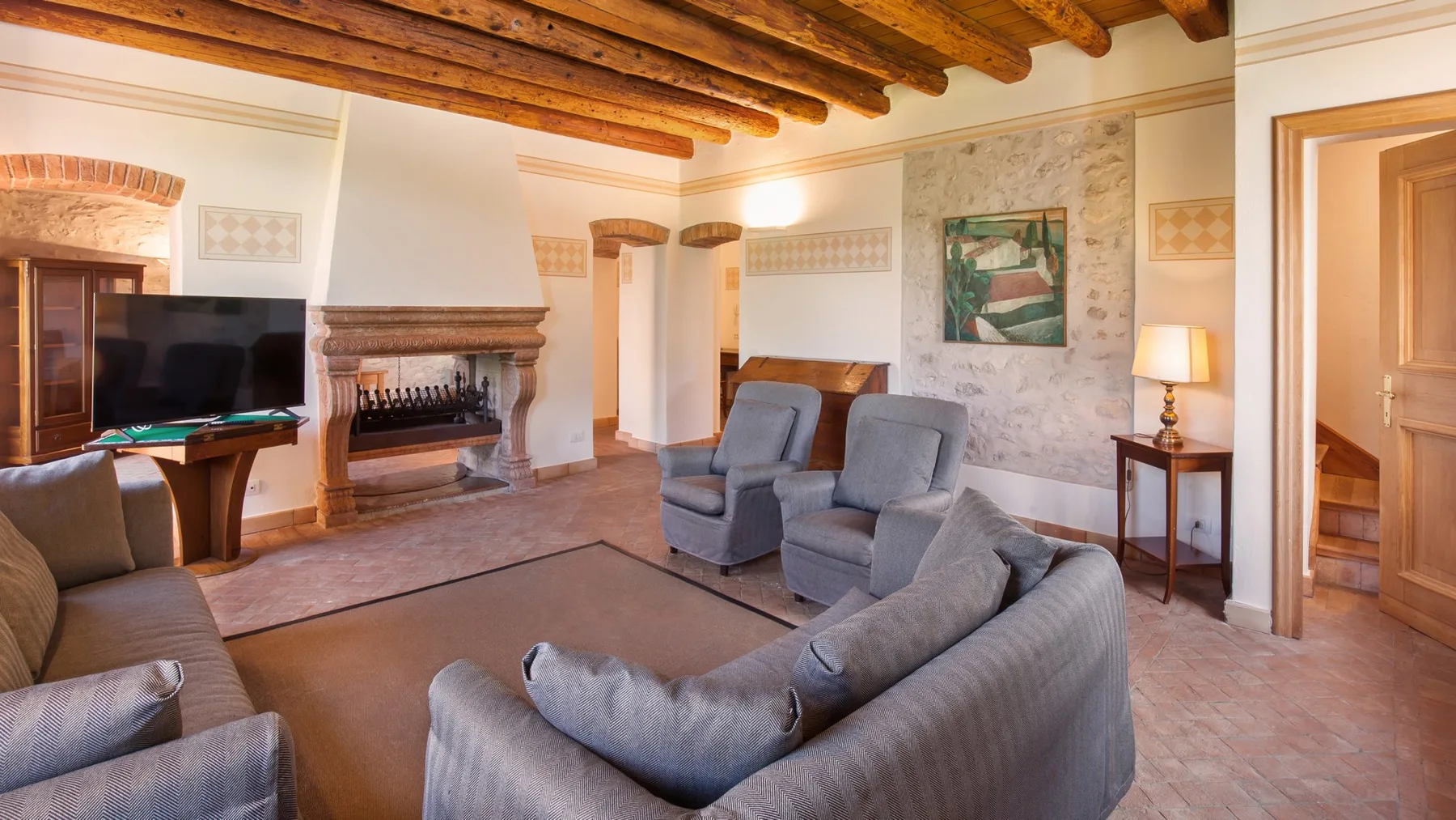 A living room with gray seating, a fireplace, and exposed wooden ceiling beams.