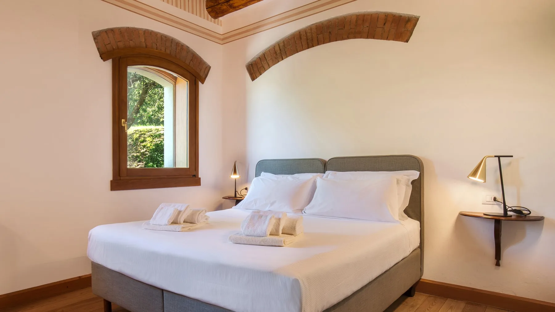 A bedroom with a double bed, white linens, and a window.