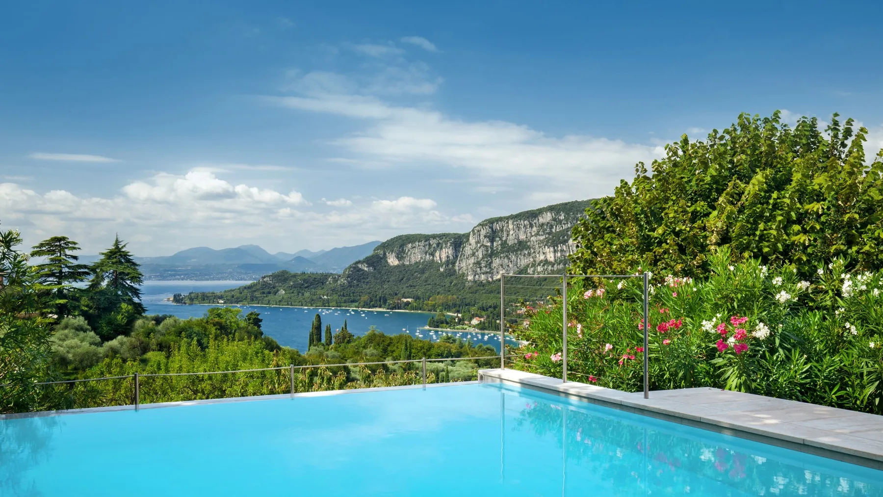 An outdoor swimming pool overlooks a lake and green hills.