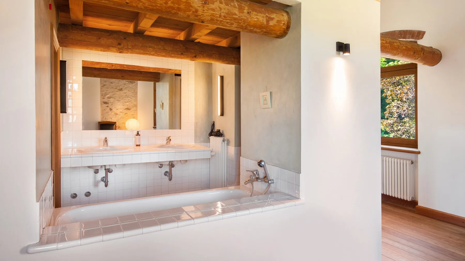 A bathroom with a built-in bathtub beneath exposed wooden beams.