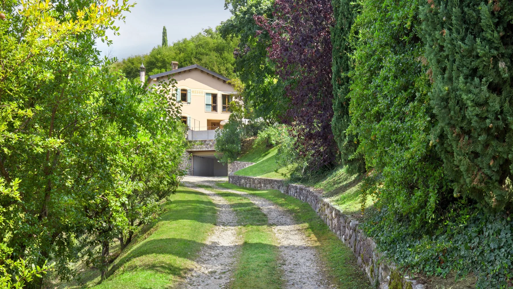 A gravel driveway runs through a leafy garden toward a pale house.
