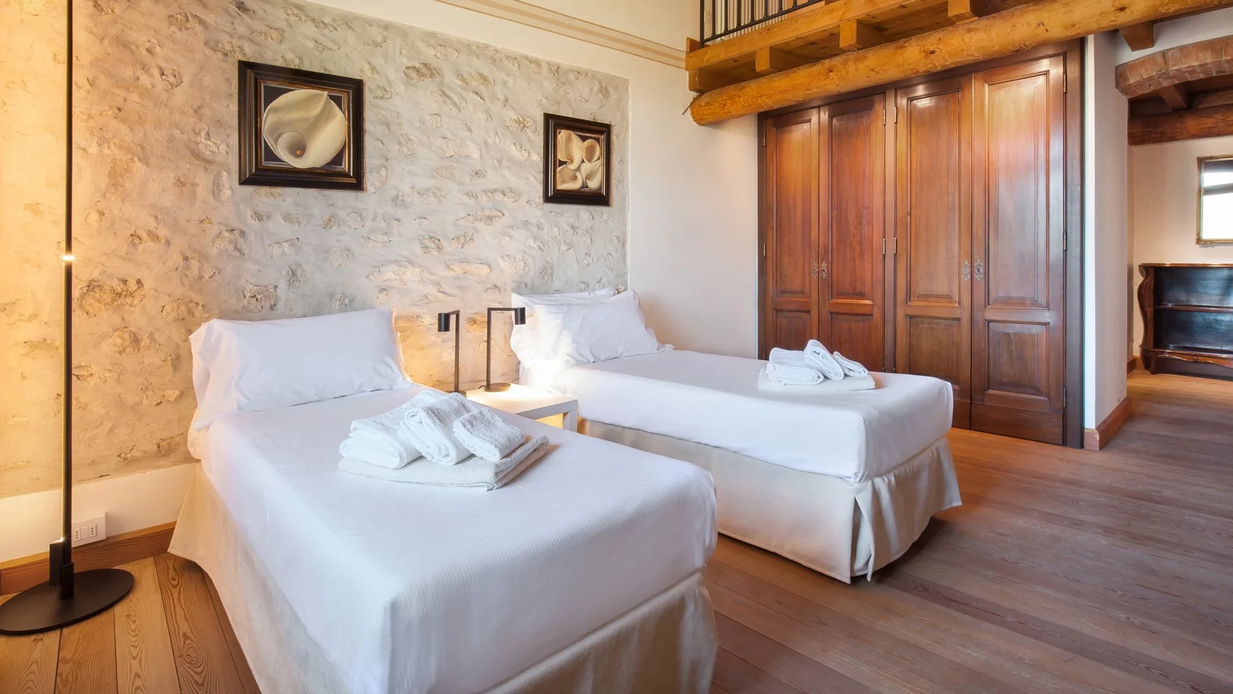 A bedroom with two beds, a stone wall, and wooden wardrobes.