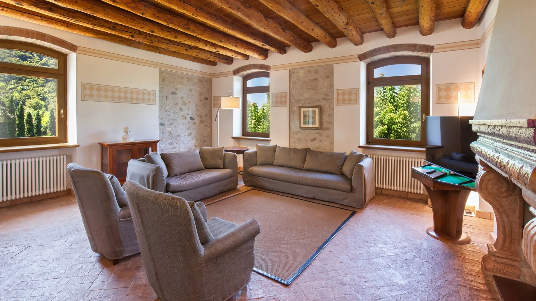 A living room with seating arranged around a rug and windows overlooking greenery.