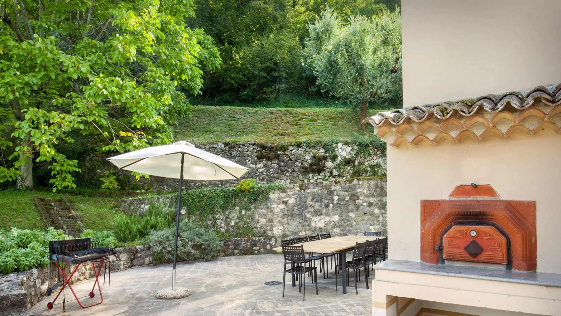 An outdoor dining patio with a table, umbrella, grill, and built-in oven.