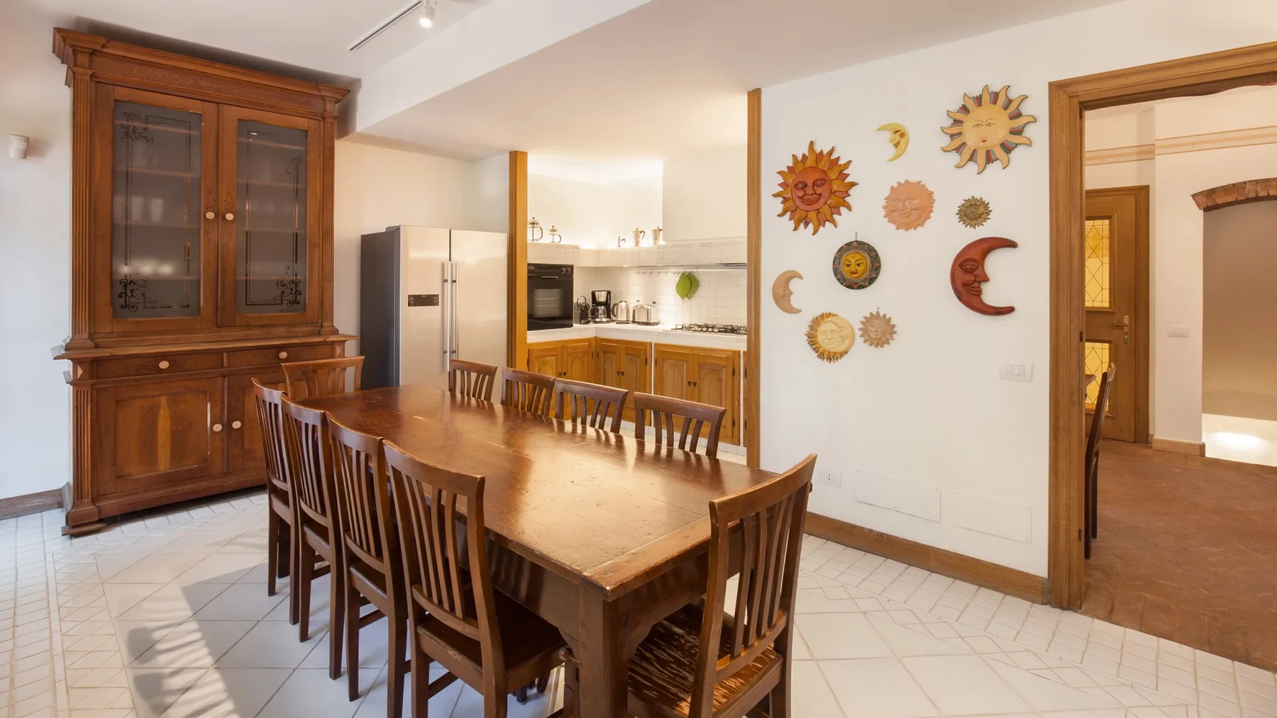 A dining area with a long wooden table and chairs beside a kitchen.