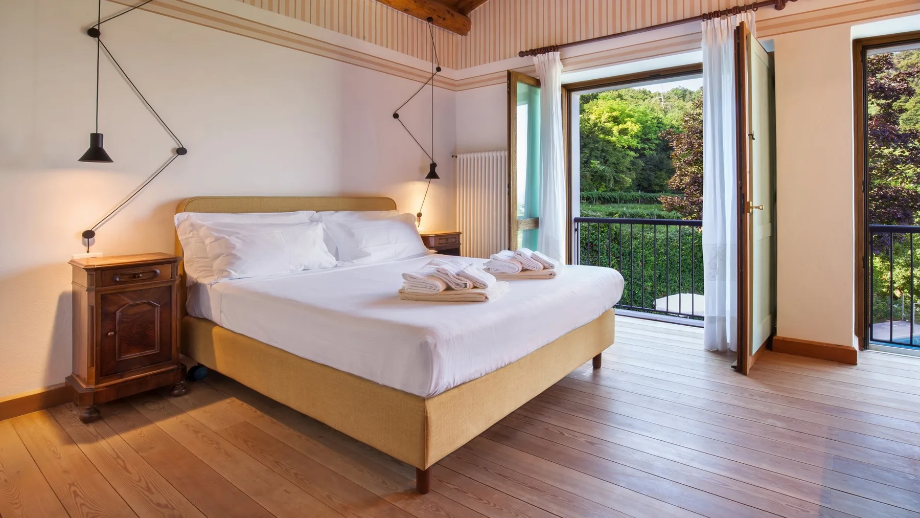 A bedroom with a neatly made bed beside open doors overlooking greenery.