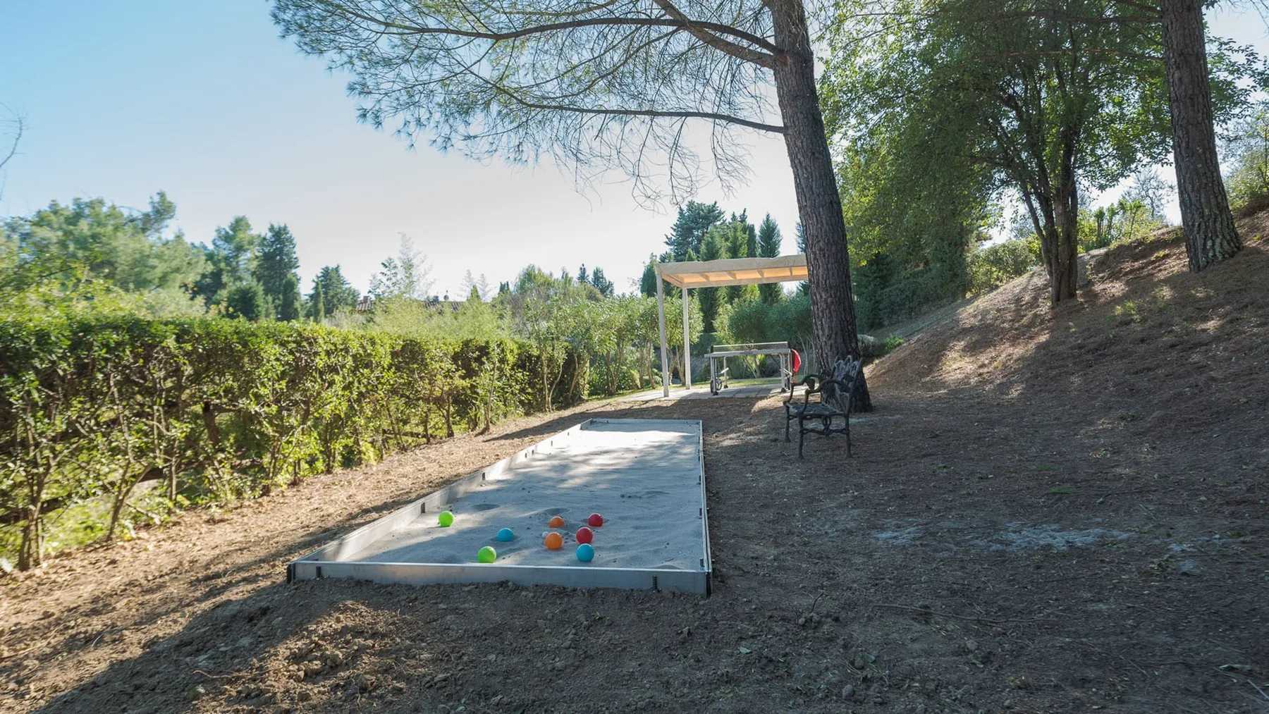 Una cancha de juego al aire libre está junto a un seto y árboles con sombra.