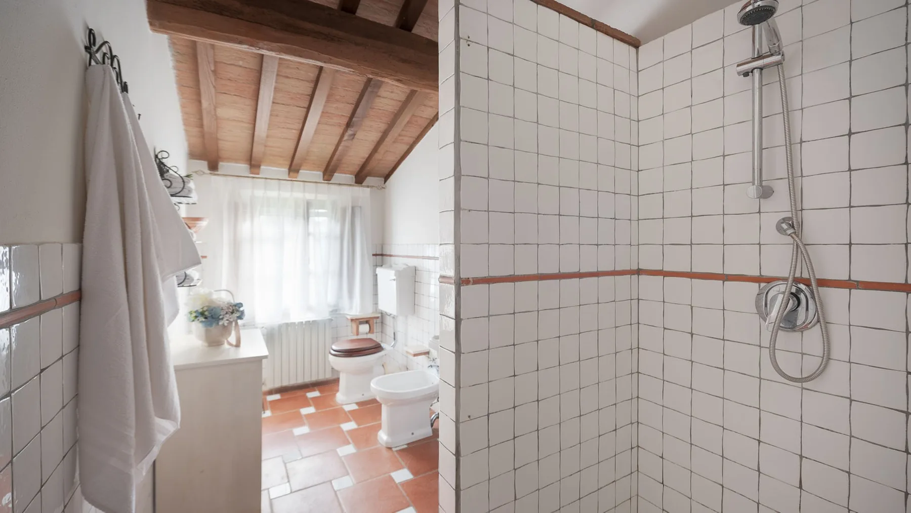 Un baño con azulejos, ducha, inodoro y ventana.