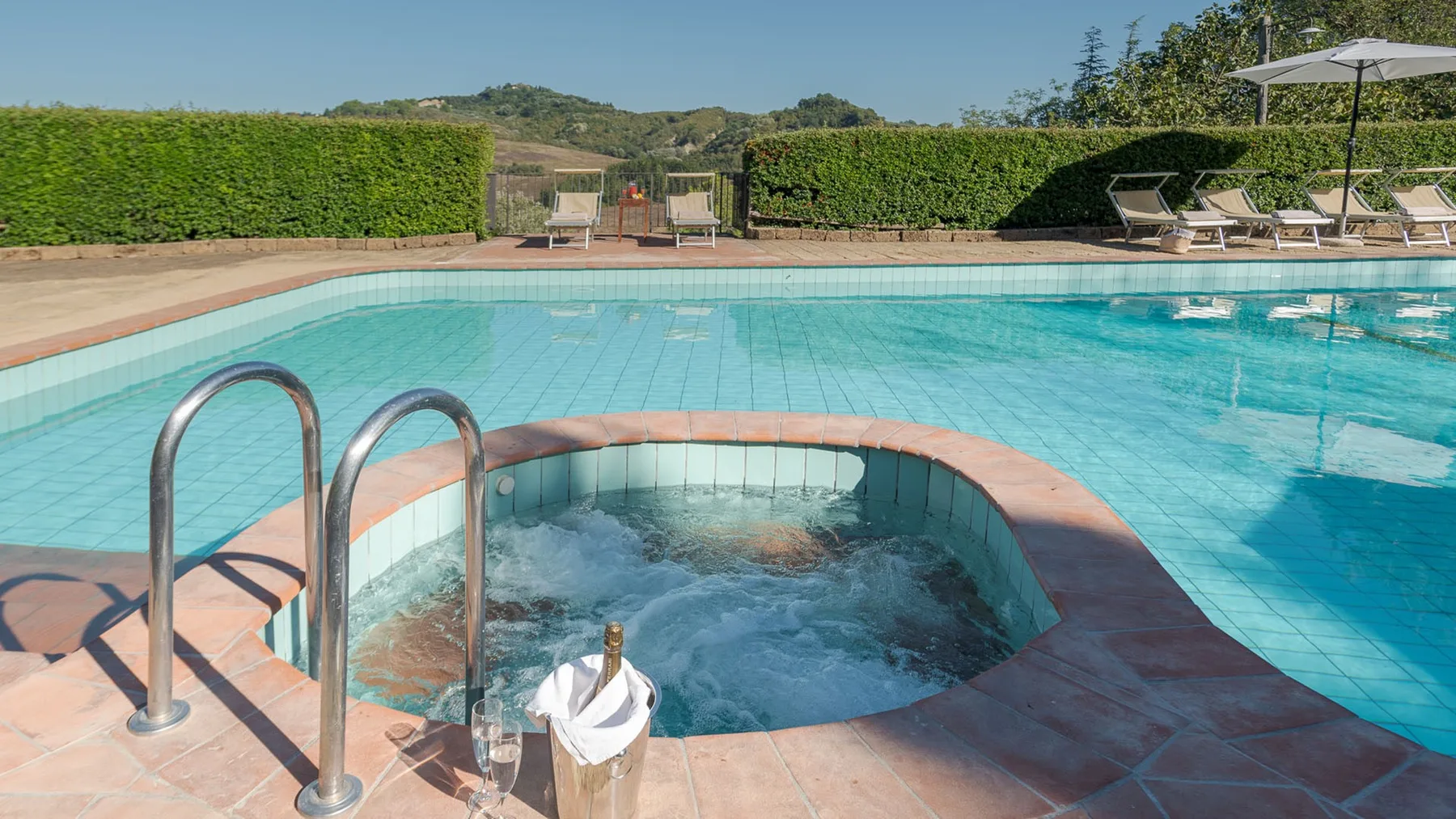 Una piscina exterior con un spa burbujeante integrado y tumbonas cerca.